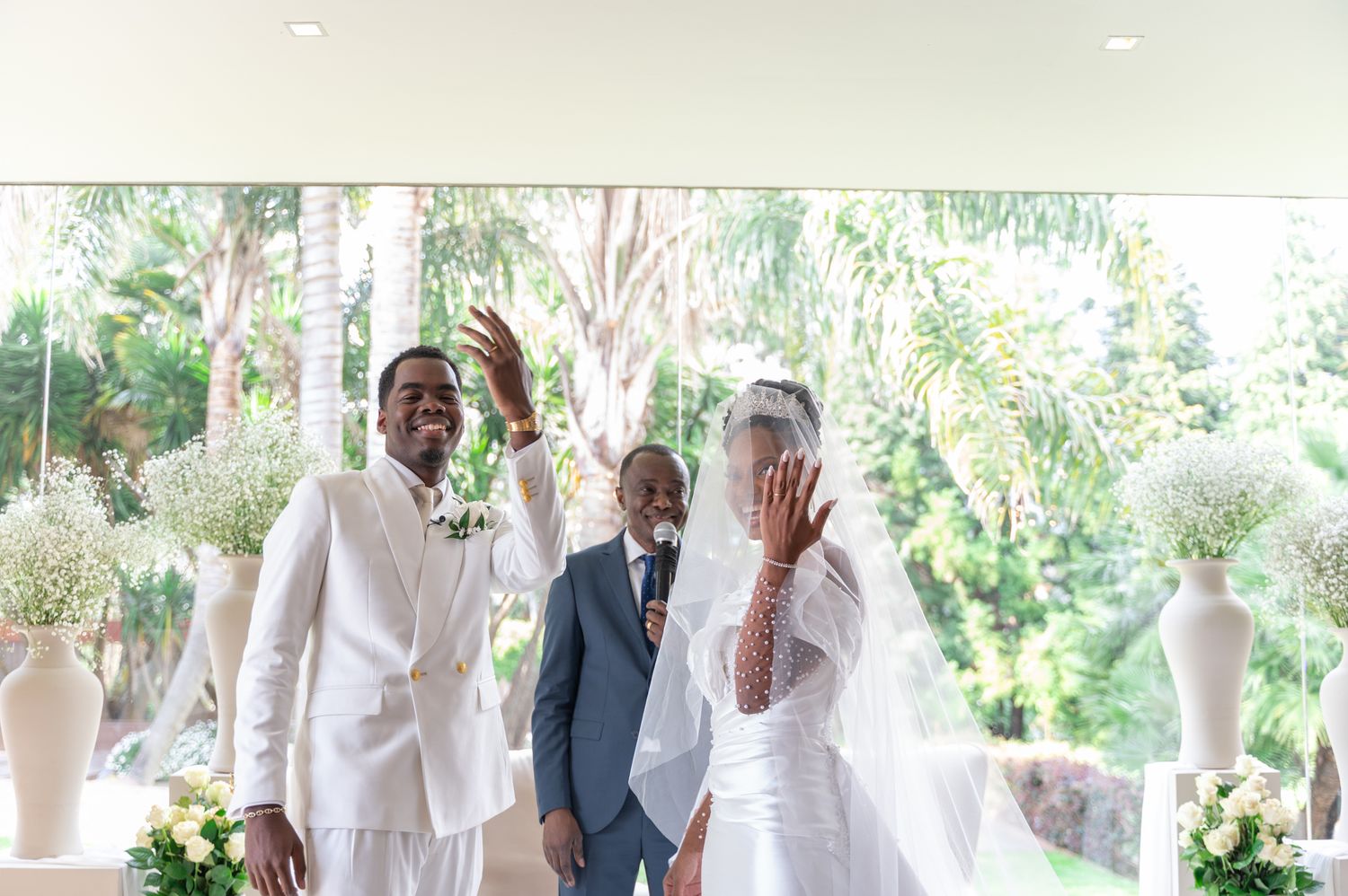 Bride and groom wave joyfully at altar as officiant stands between them at wedding.