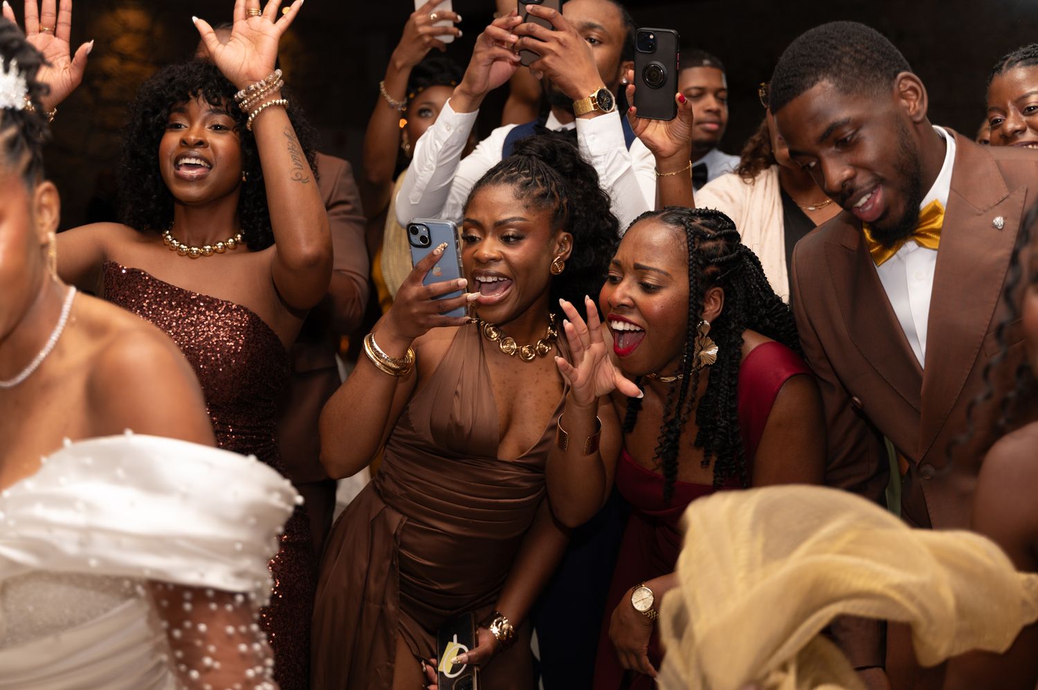 Joyful wedding guests in brown and gold attire dancing and celebrating at a lively wedding reception.