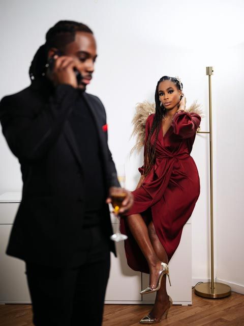 A woman in a red dress leans against a gold lamp post while a man in a black suit talks on the phone.