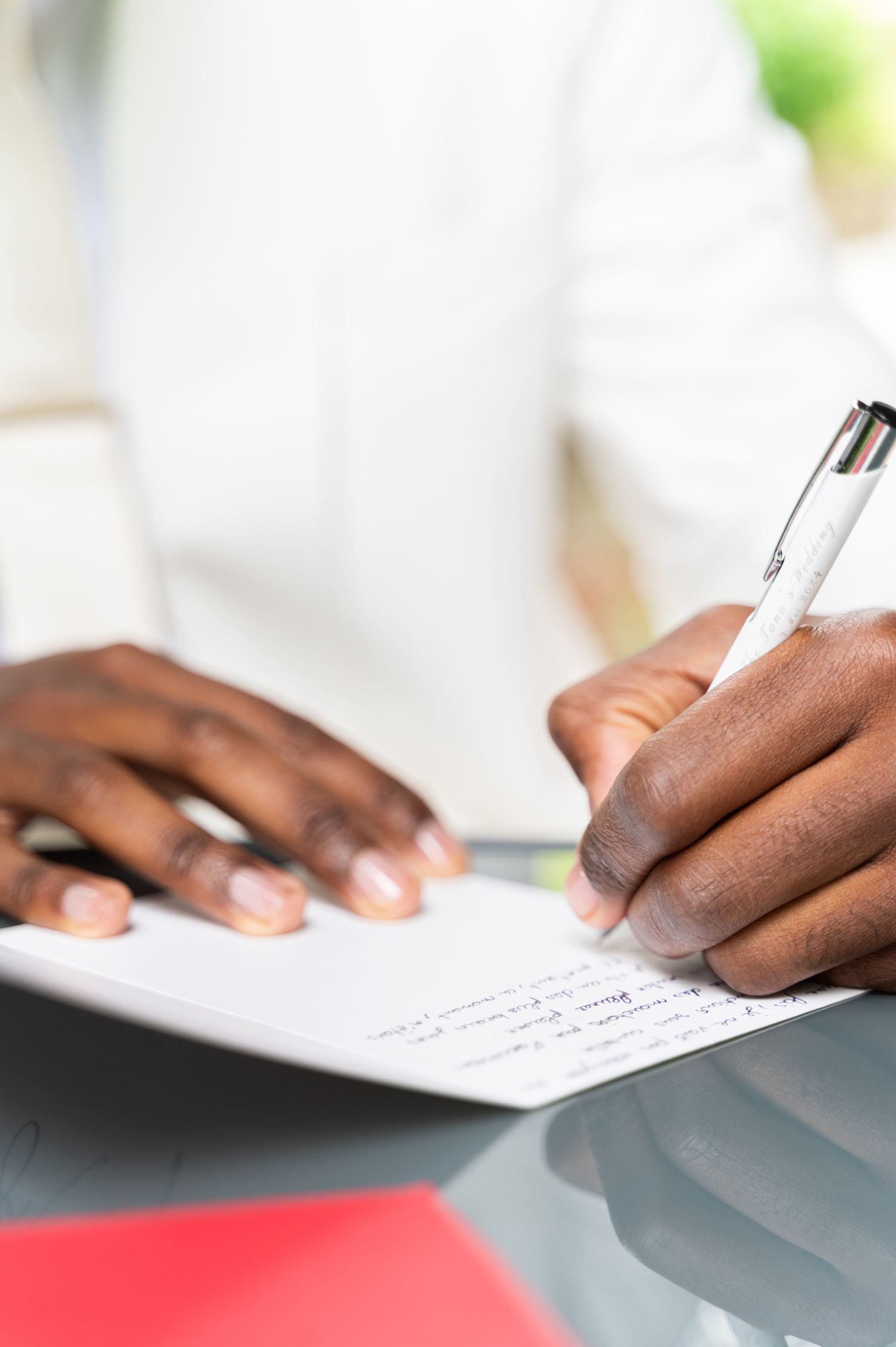 Close-up of hands writing wedding vows on paper with white pen in white suit.