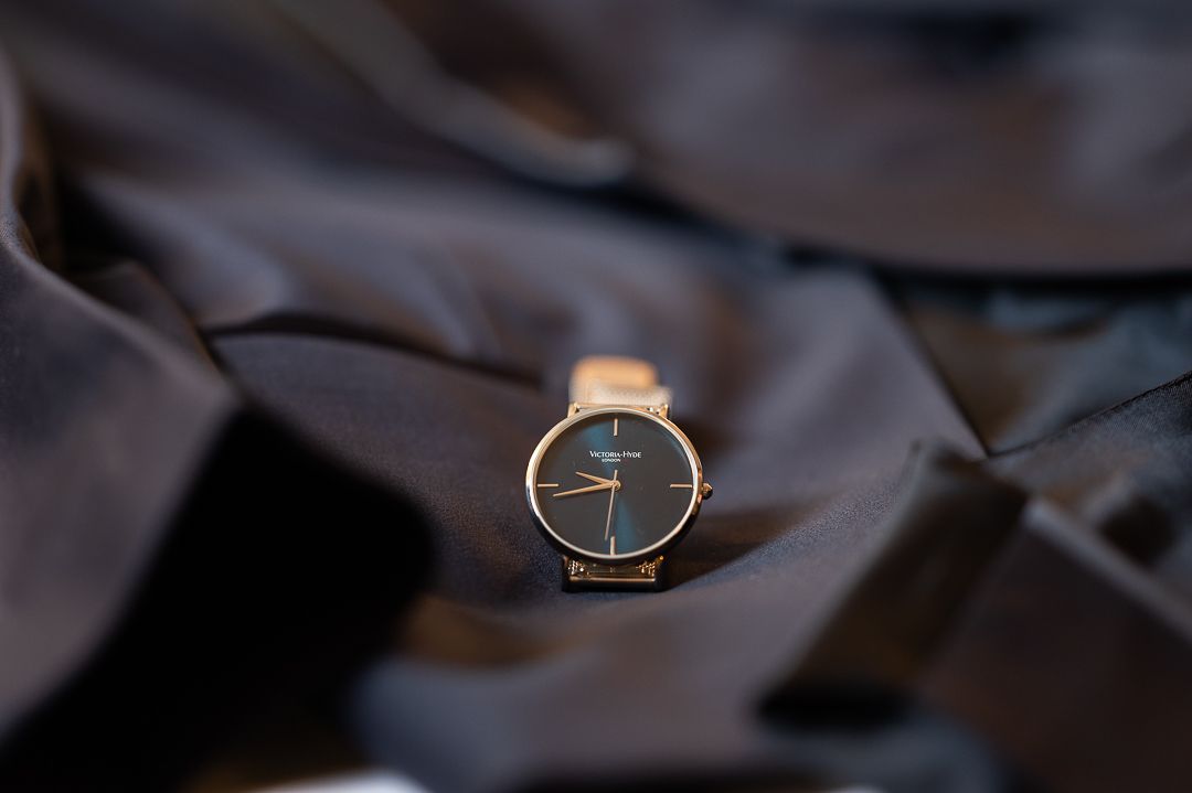 Elegant rose gold minimalist watch resting on dark fabric background.