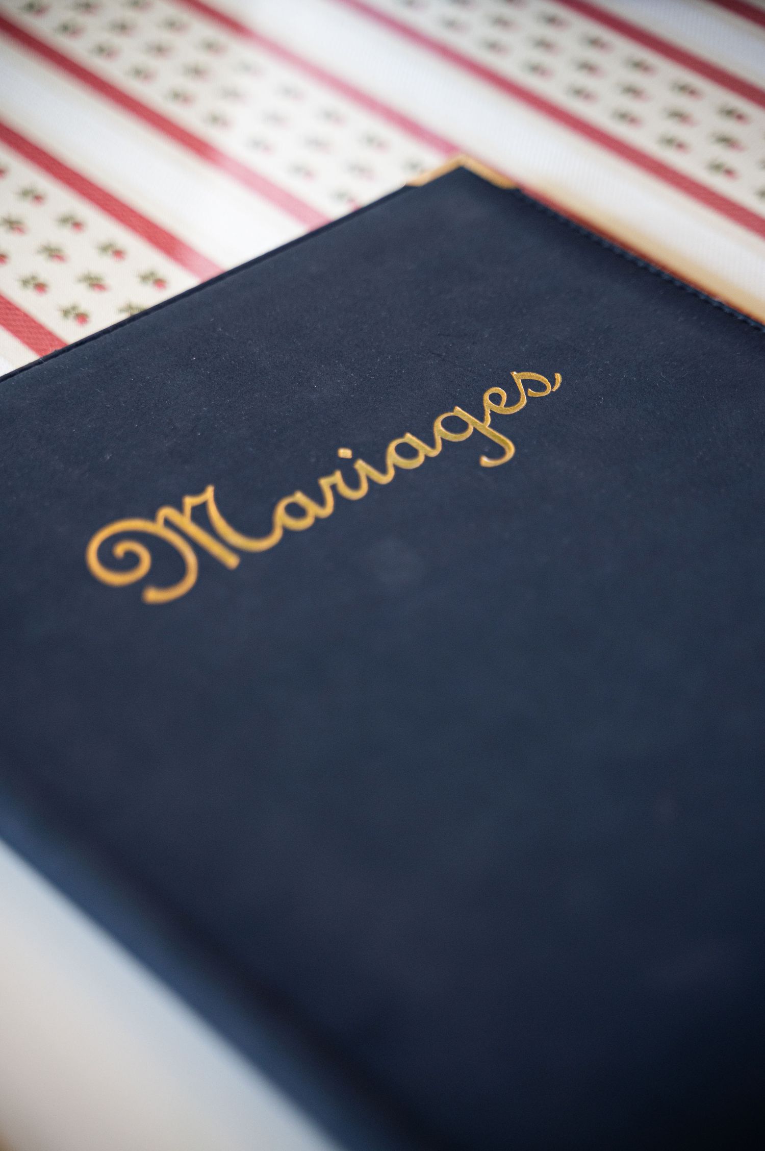 Navy blue Mariages registry book with gold script lettering on striped tablecloth.