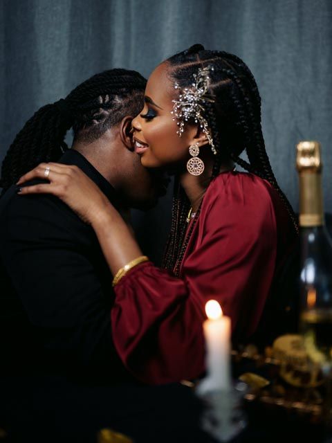 A romantic couple sharing a kiss by candlelight, with champagne nearby, dressed elegantly for a special occasion.
