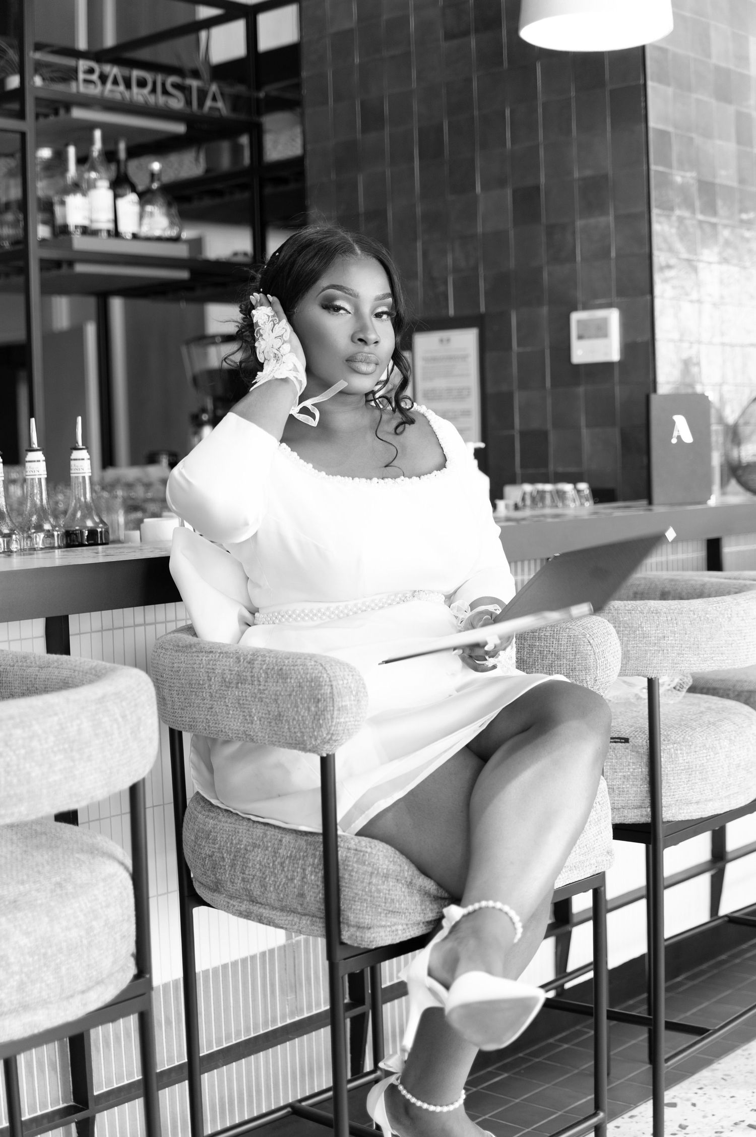Black and white photo of a woman in white dress sitting at a bar with headphones and tablet.