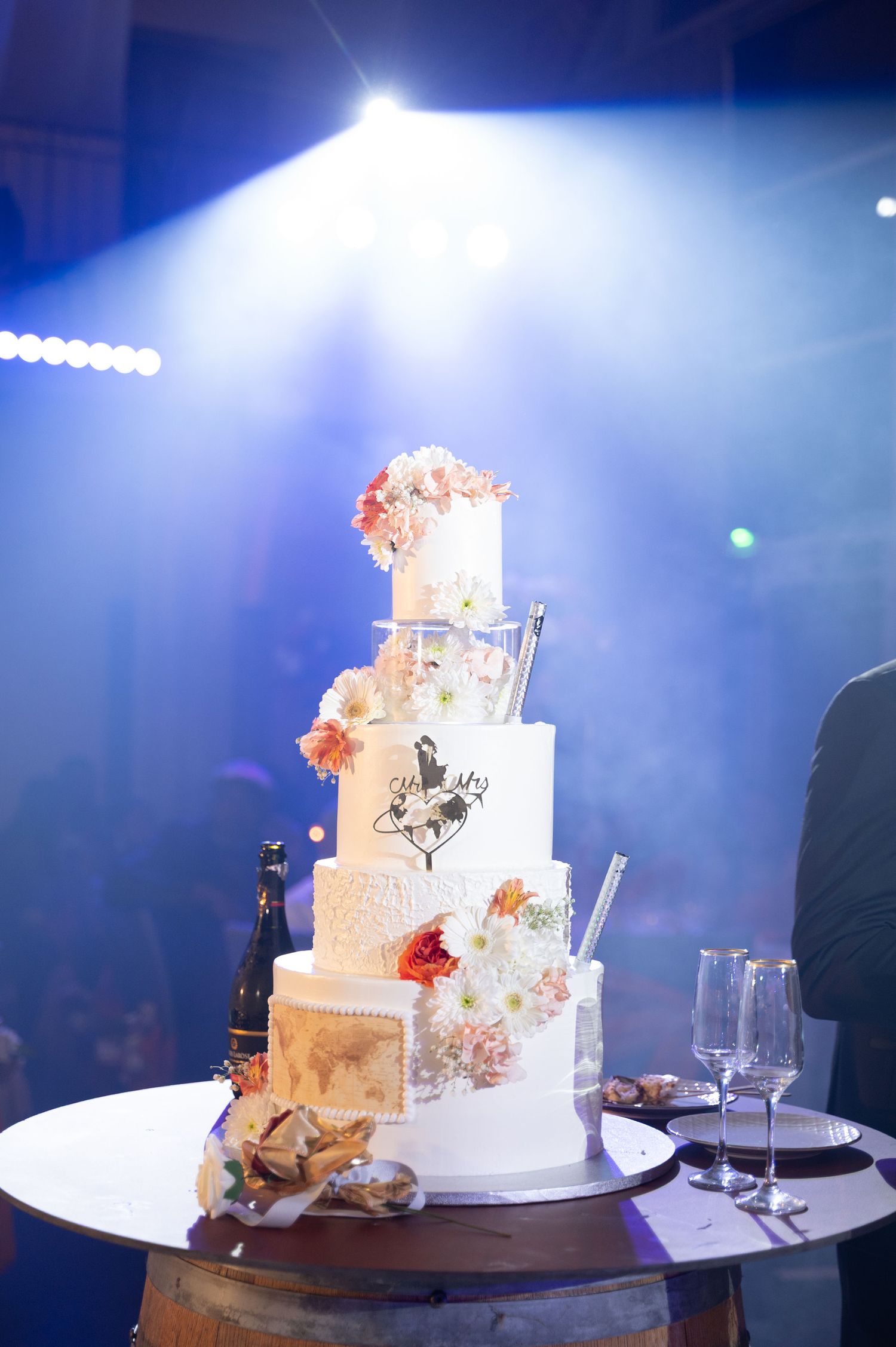 Stunning five-tier white wedding cake with floral decorations illuminated by blue spotlight at evening reception.