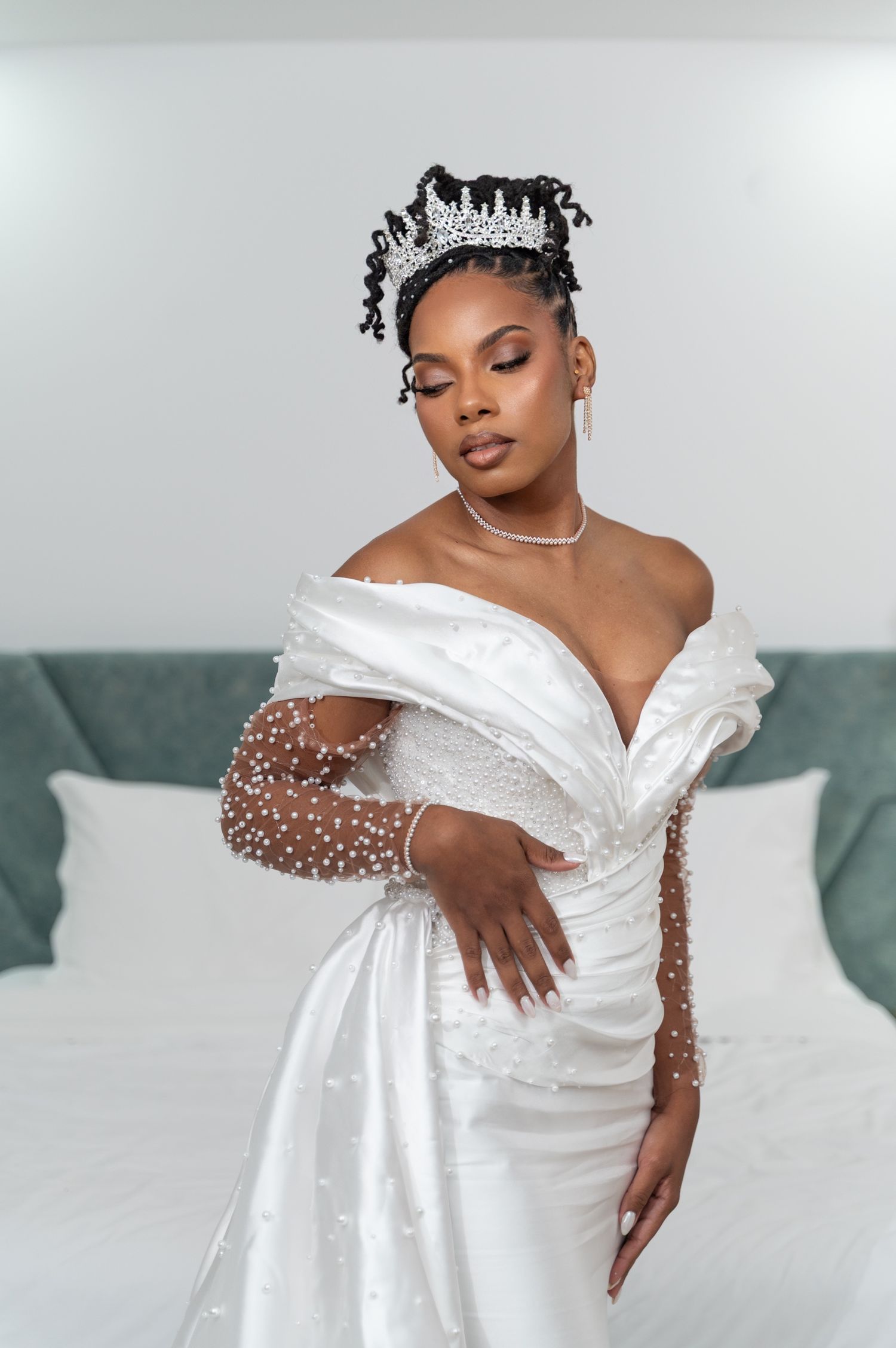 Beautiful Black bride in pearl-embellished wedding gown and crown poses gracefully.