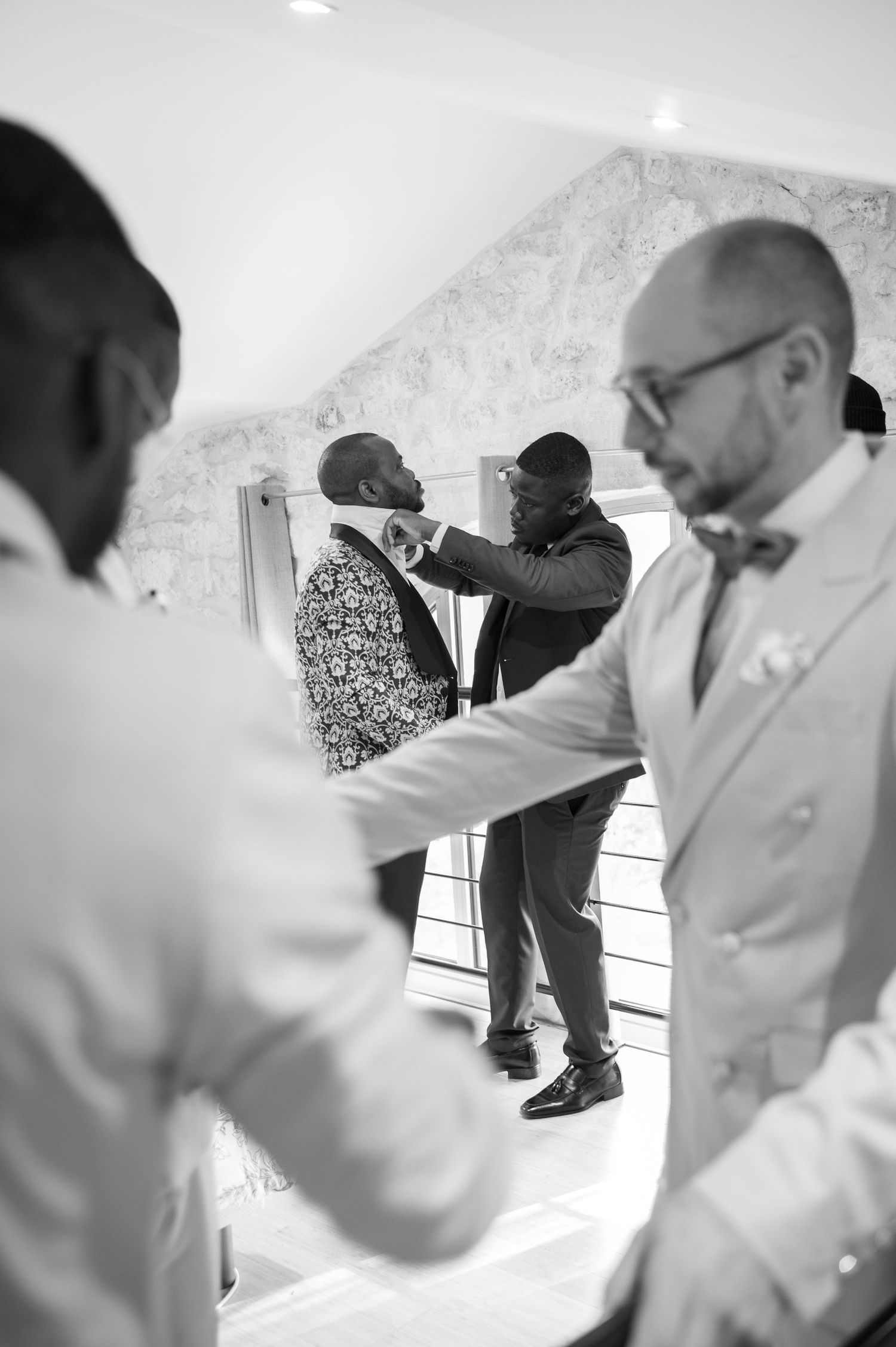 Black and white photo of groomsmen helping each other get dressed before a wedding ceremony.