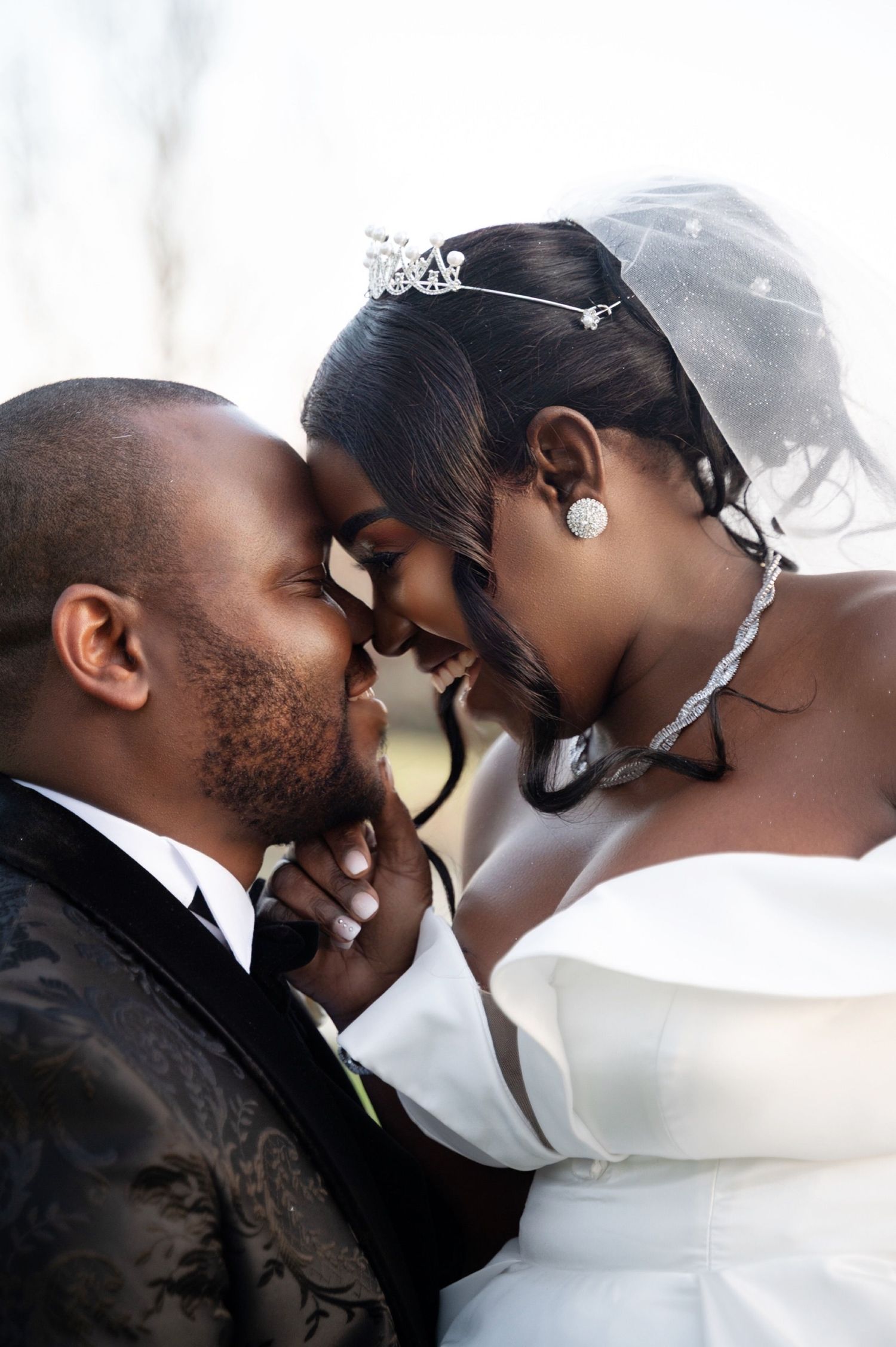 A bride and groom in elegant wedding attire share an intimate forehead-to-forehead moment, radiating love and joy.