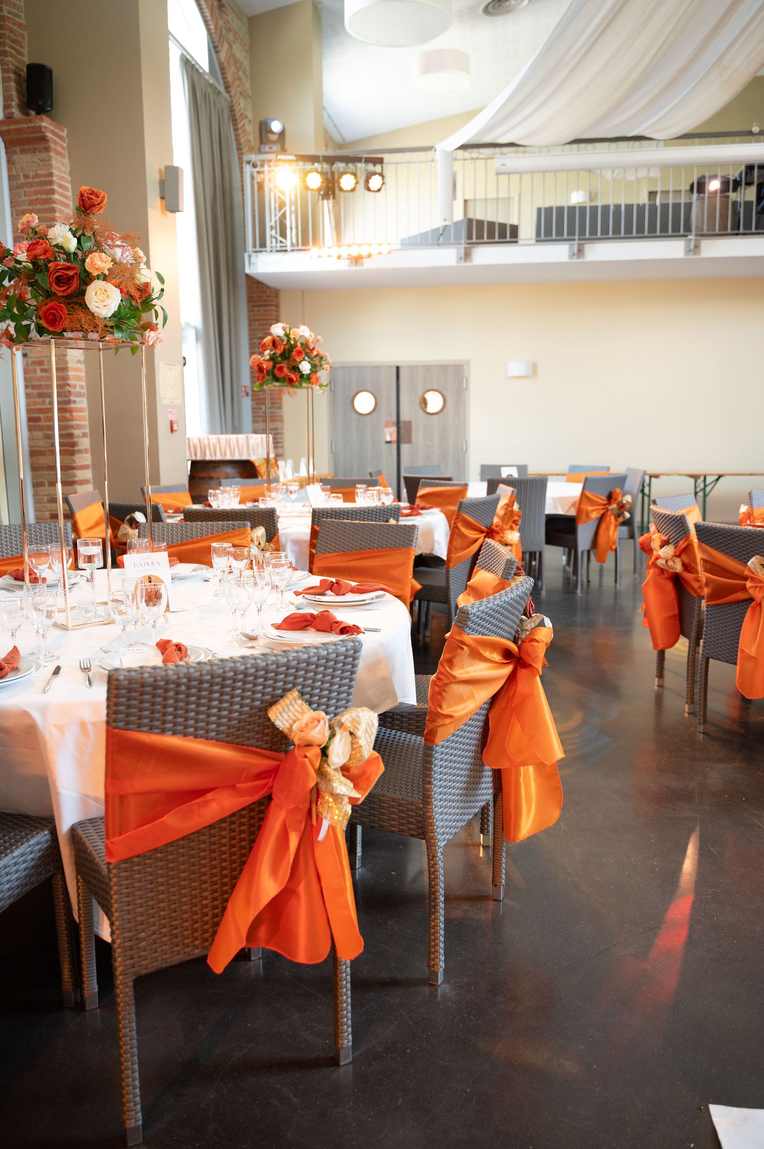 Elegant wedding reception hall decorated in orange and white with floral centerpieces and draped ceiling.