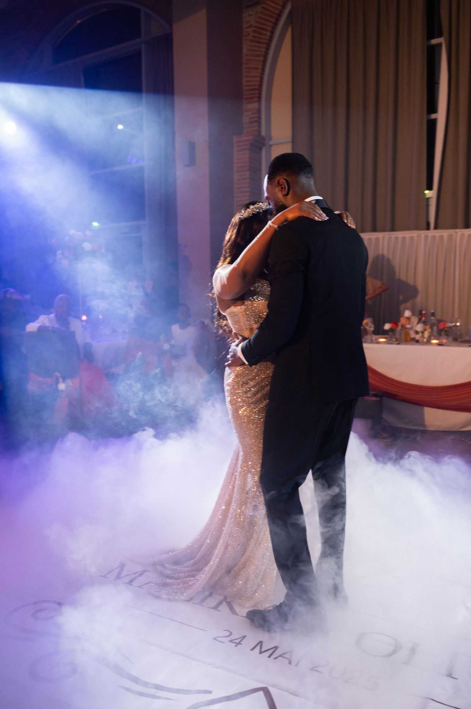 Newlyweds share an intimate slow dance on a foggy dance floor with dramatic blue stage lighting at their wedding.