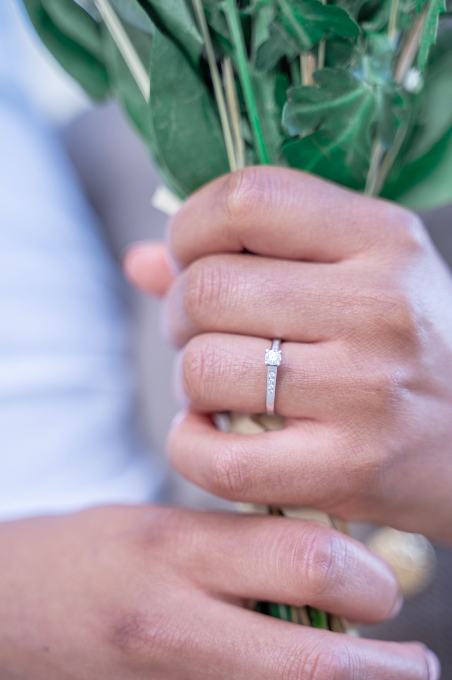 Close-up of elegant diamond engagement ring on finger holding green bouquet.