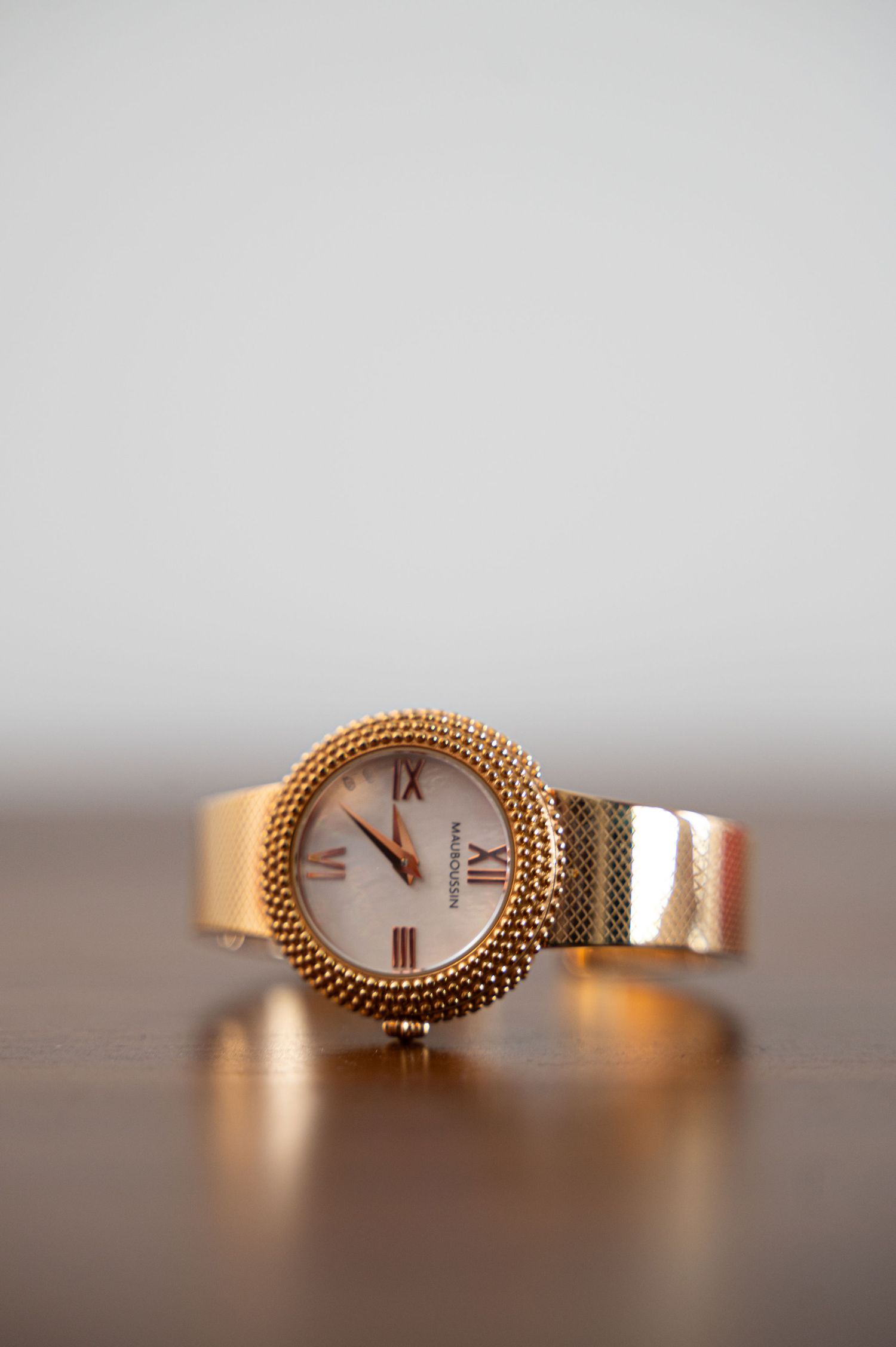 Rose gold women's wristwatch with beaded bezel and Roman numerals displayed on wooden surface.