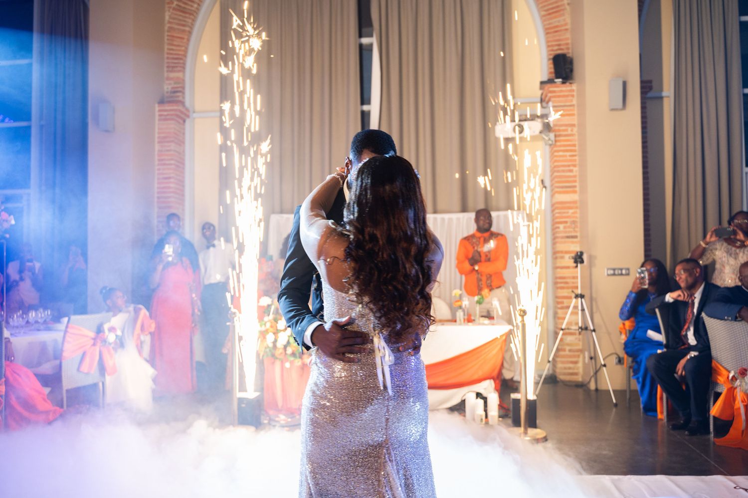 Newlyweds kiss on a foggy dance floor surrounded by sparkling cold fireworks at their stunning wedding reception.
