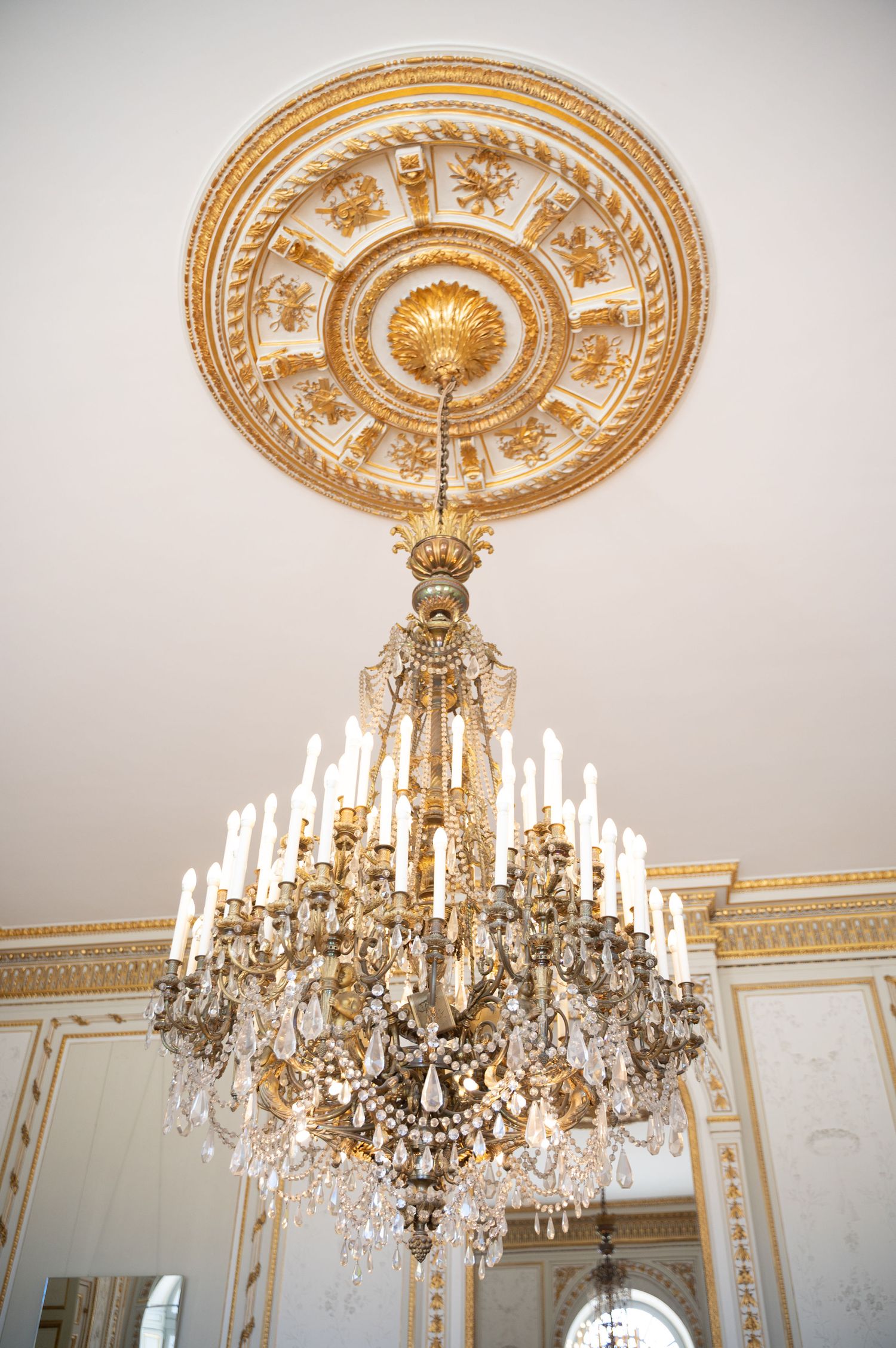 Ornate gold crystal chandelier hanging from decorative ceiling medallion in elegant wedding venue.
