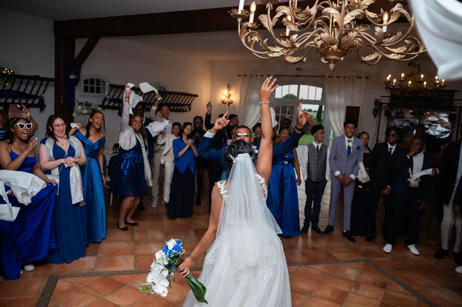 Joyful bride tosses bouquet to bridesmaids in royal blue gowns at wedding reception.