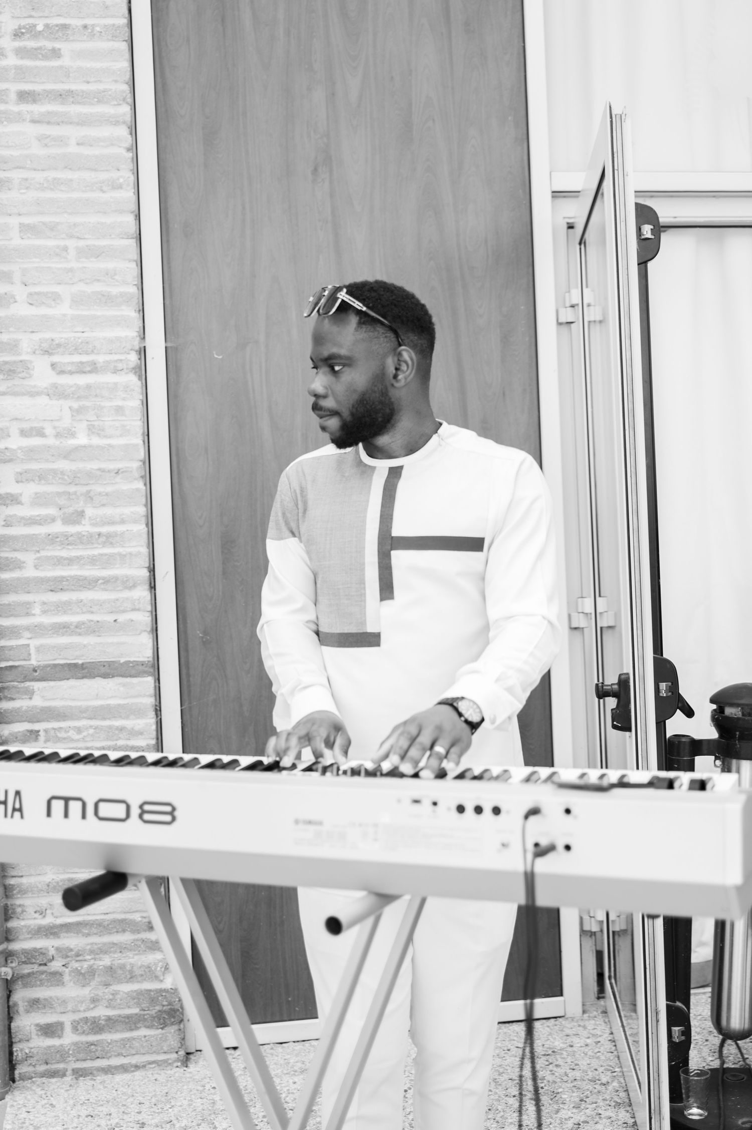 Black and white photo of man playing Yamaha MO8 keyboard synthesizer at outdoor wedding event.