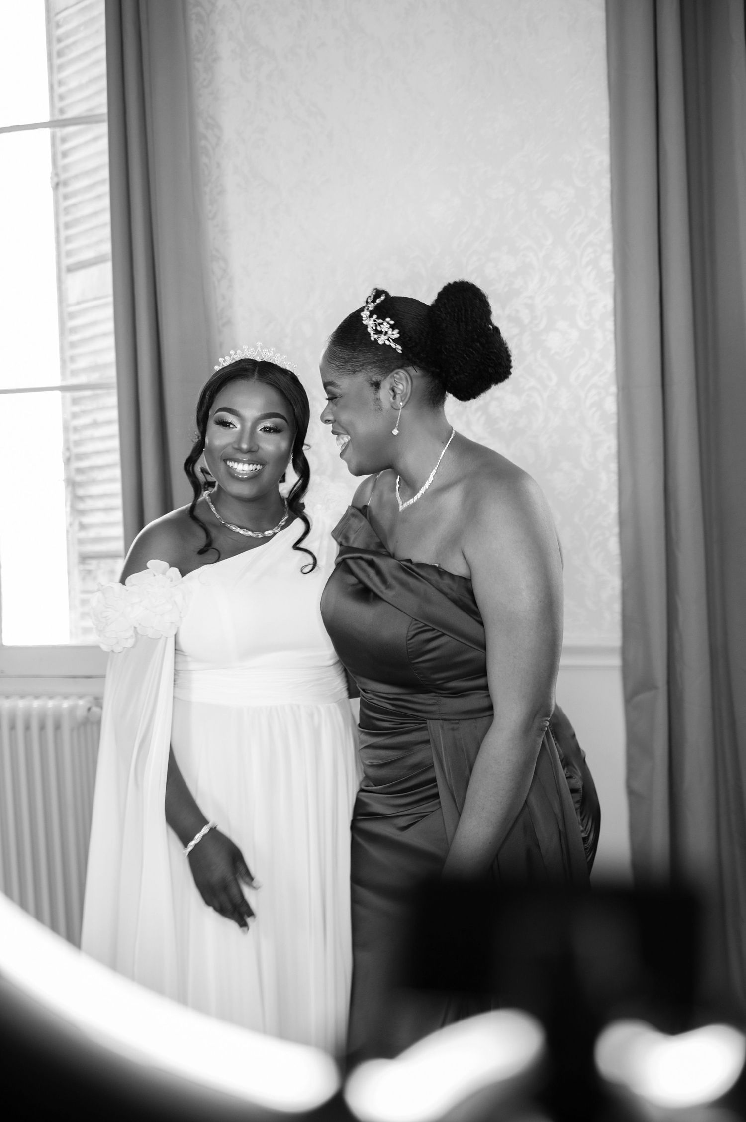 Black and white photo of a smiling bride in white gown with bridesmaid in elegant dark dress at wedding.