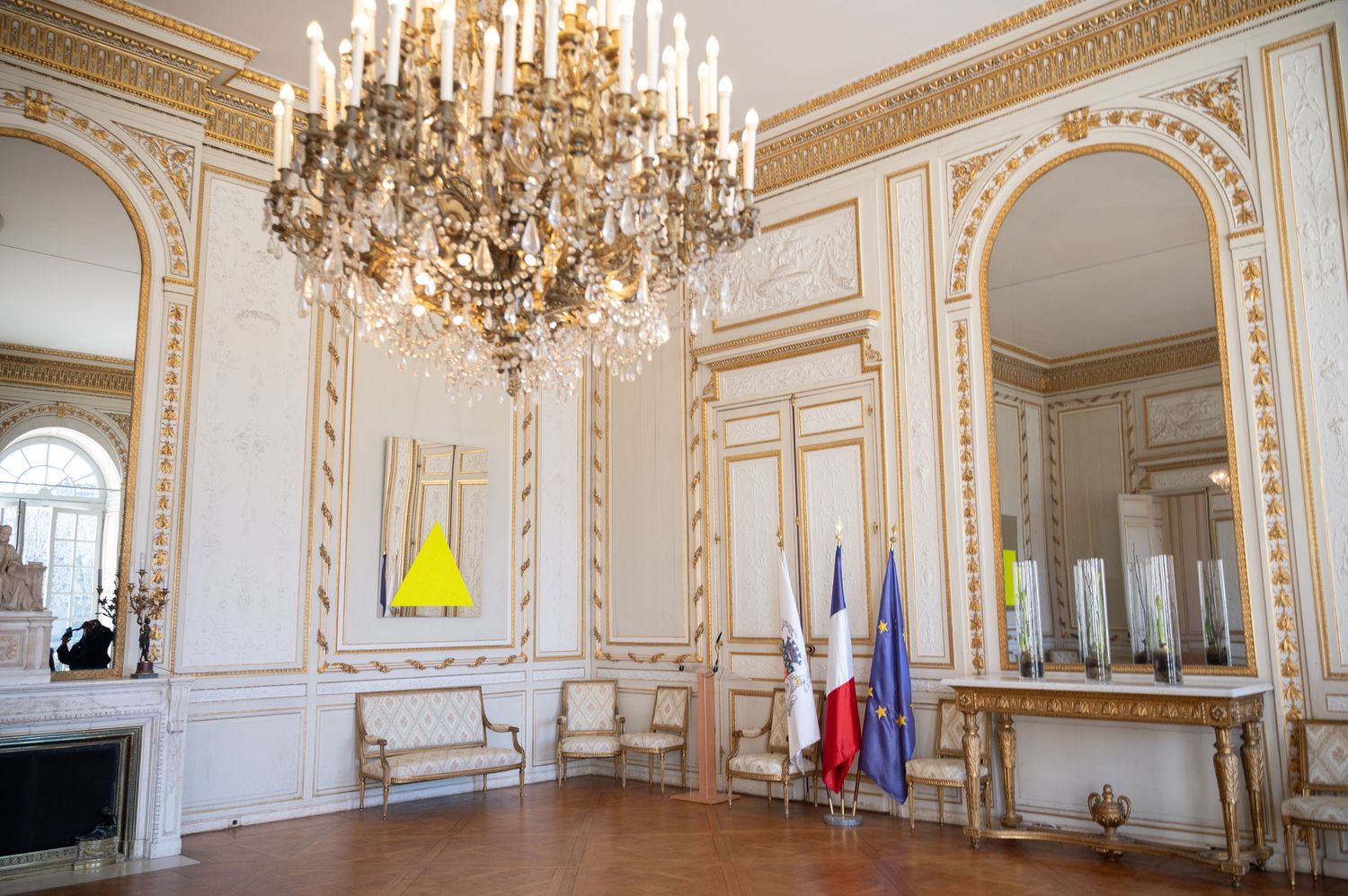 Ornate French wedding venue room with gold chandelier, white walls, and French flags on display.