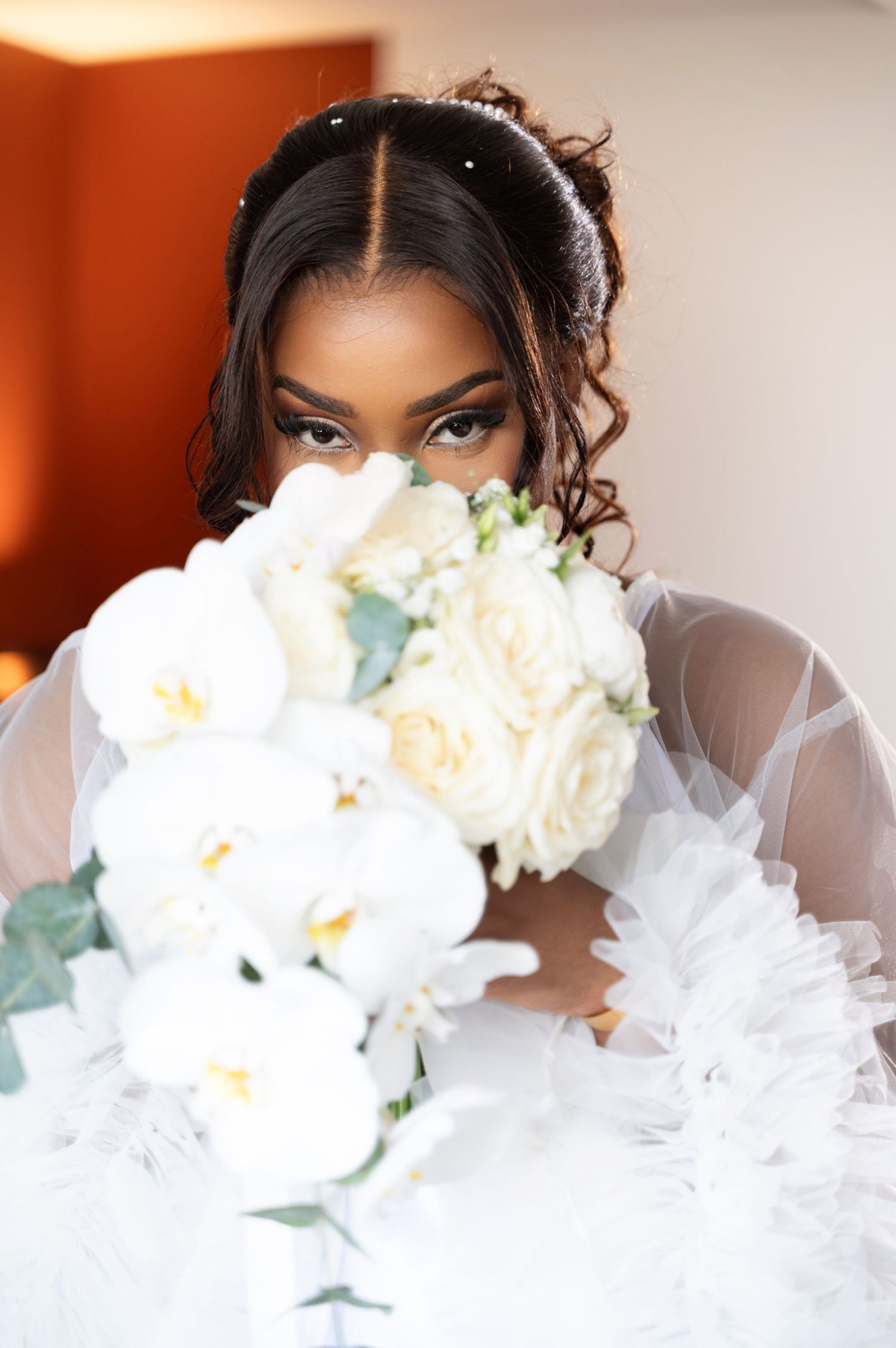 Beautiful bride with glamorous makeup partially hiding face behind white orchid bridal bouquet.