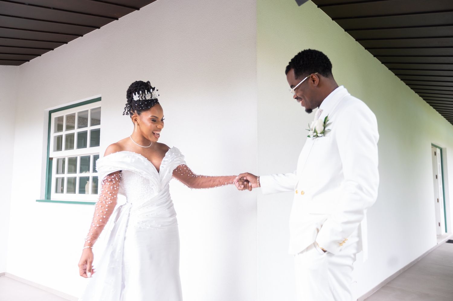 Bride and groom in white attire hold hands outdoors, sharing a joyful first look moment on their wedding day.
