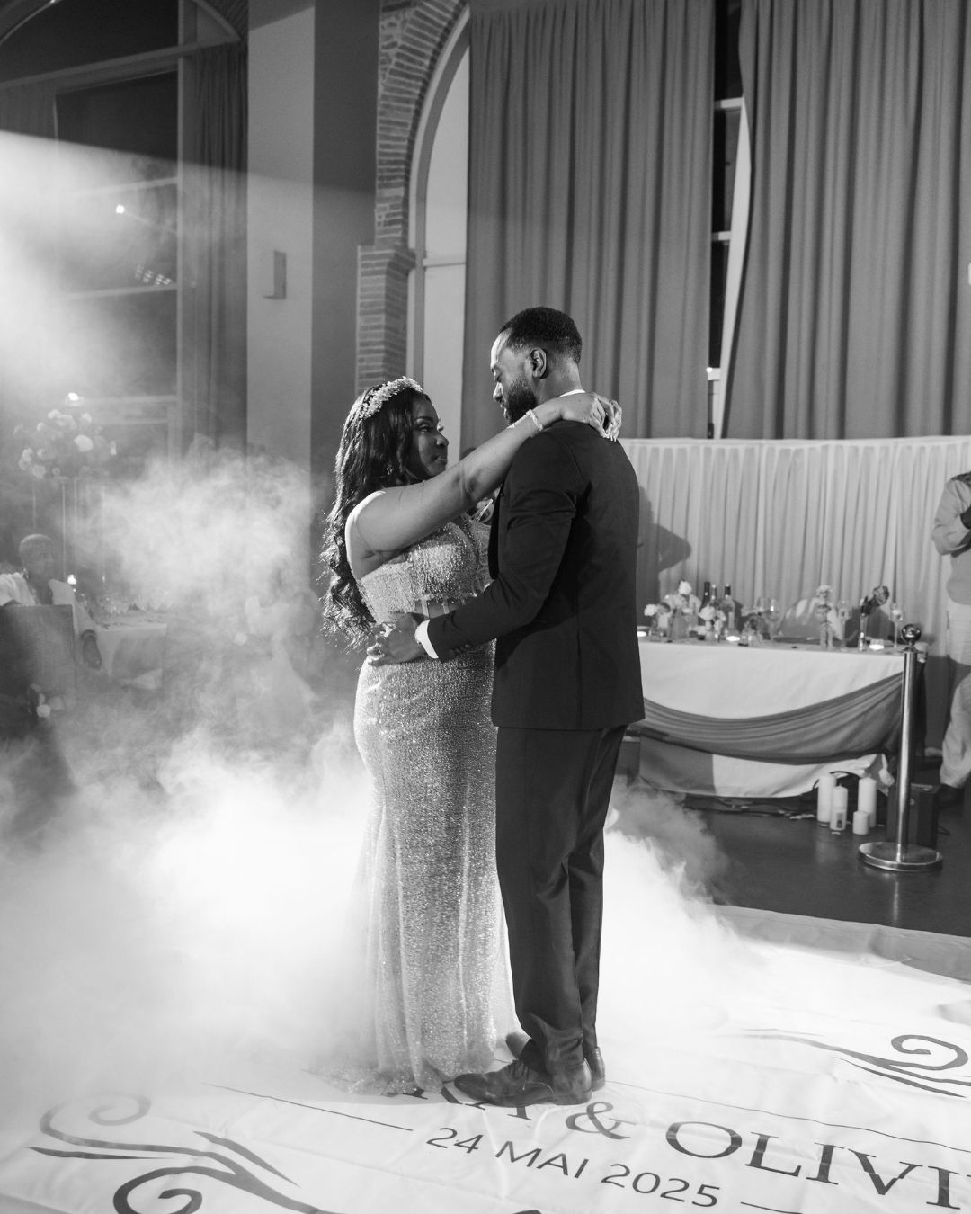 Black and white photo of newlyweds sharing their first dance on a foggy dance floor dated 24 Mai 2025.