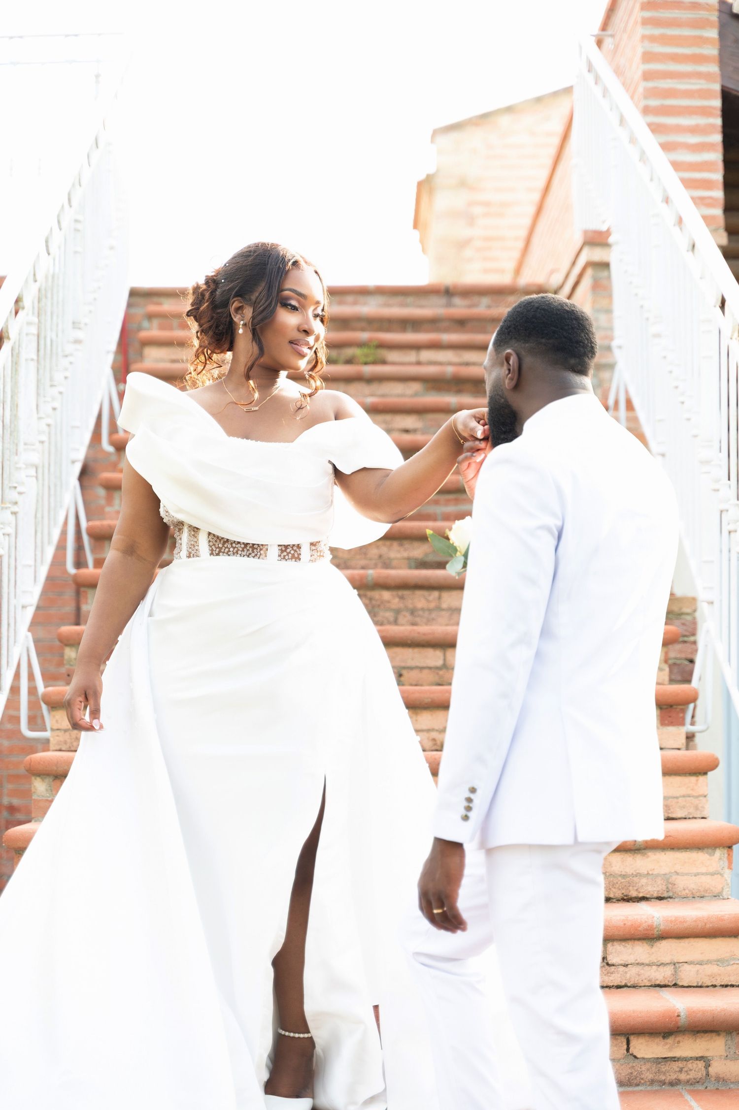 Joyful bride in white wedding gown smiling at groom while descending decorative brick staircase together.