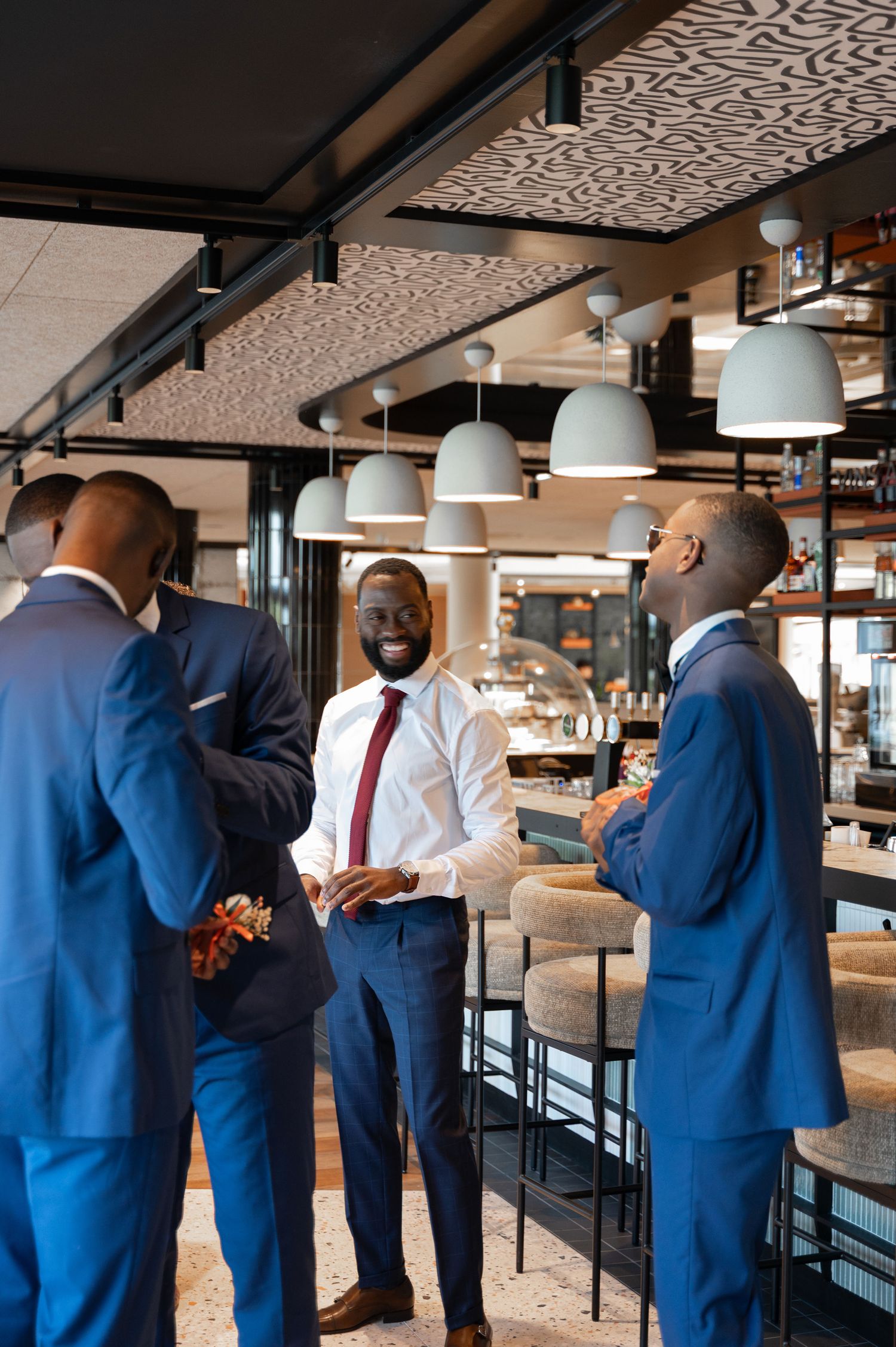 Group of stylish Black groomsmen in navy blue suits socializing and smiling in an elegant bar setting.