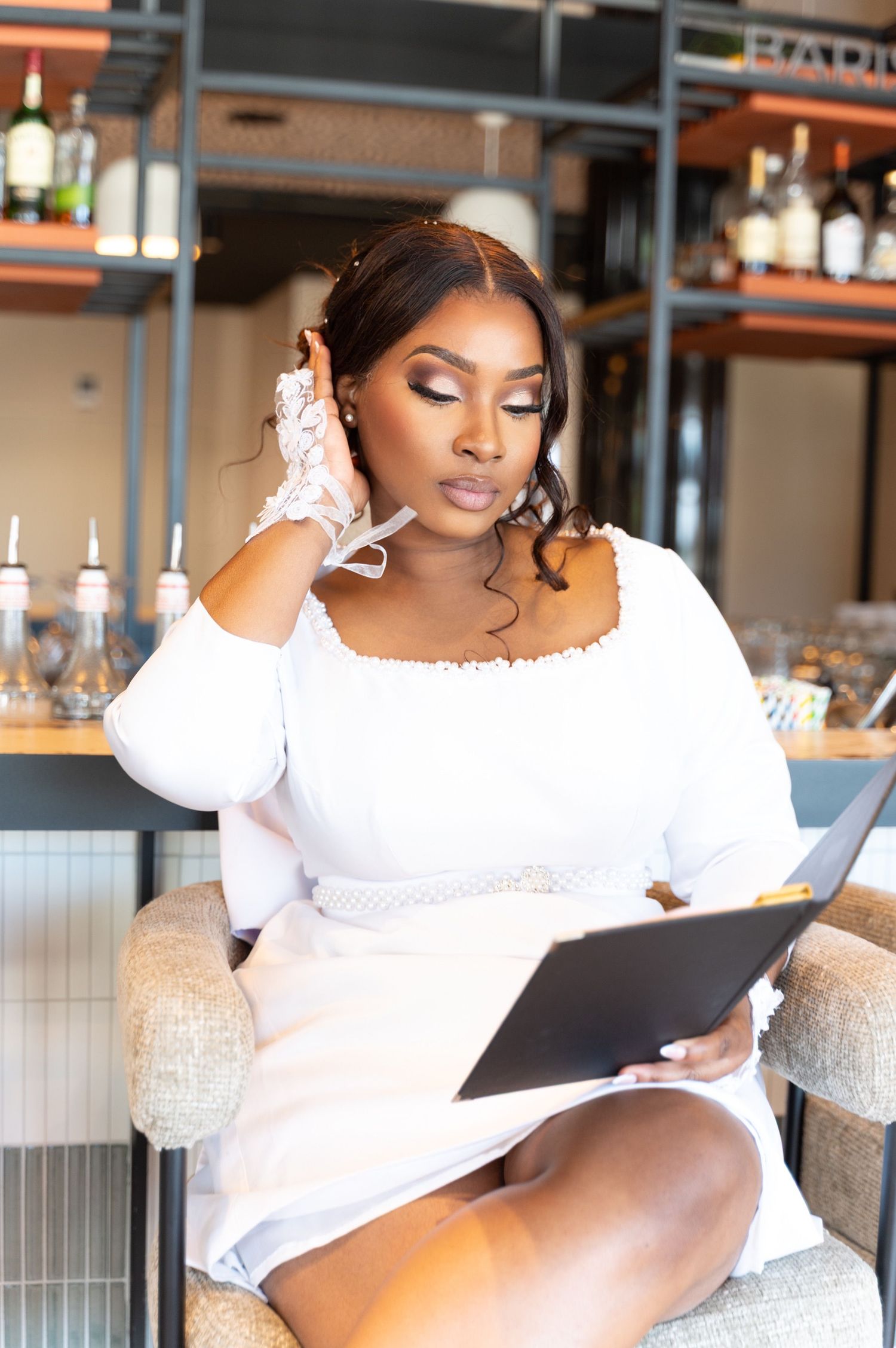 Elegant woman in white off-shoulder dress reading a menu at a stylish bar restaurant.