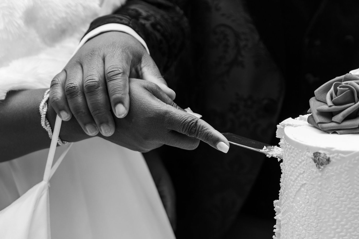 Black and white close-up of bride and groom cutting wedding cake together at reception.
