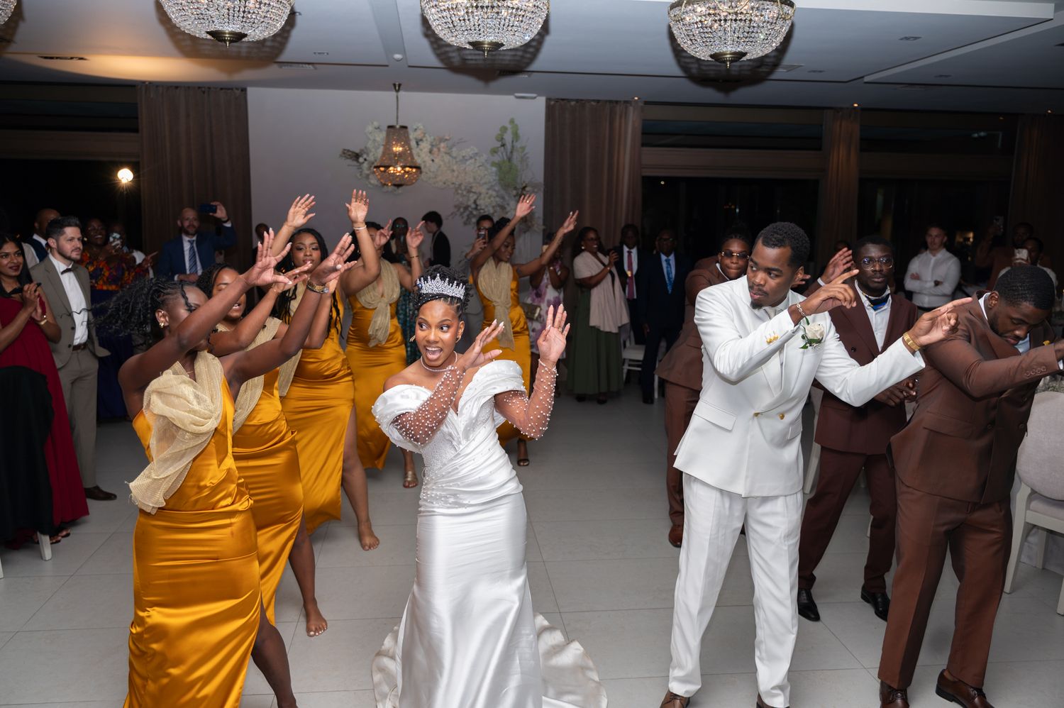 Bride and groom lead an energetic wedding reception dance with bridesmaids in gold dresses and groomsmen.
