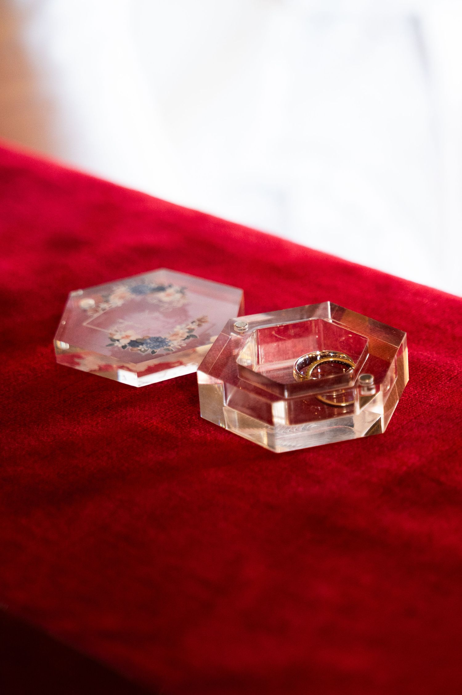 Gold wedding rings presented in an open hexagonal clear acrylic box on a red velvet surface.