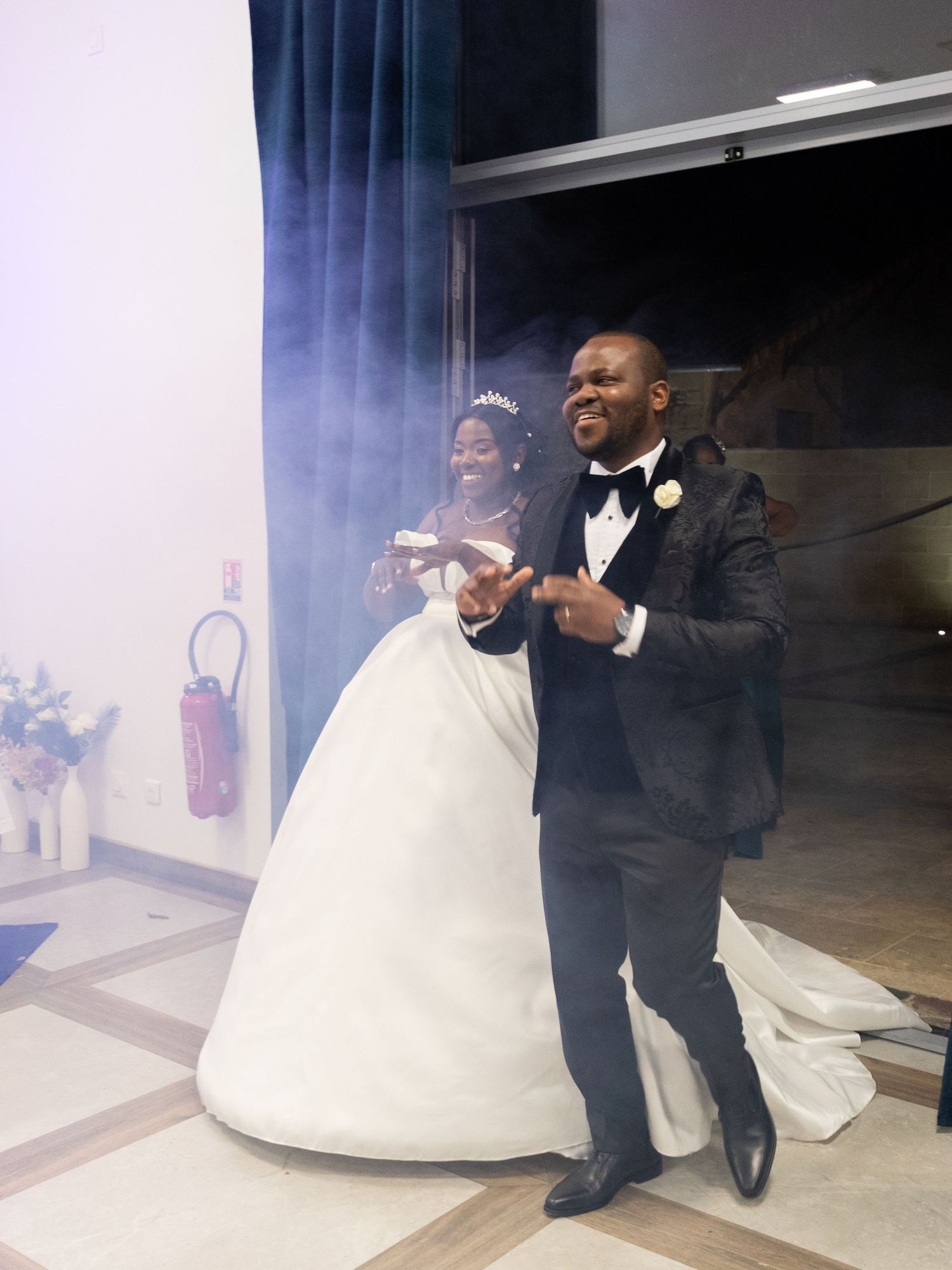 Bride in ballgown and groom in black tuxedo making grand entrance at wedding reception with smoke.