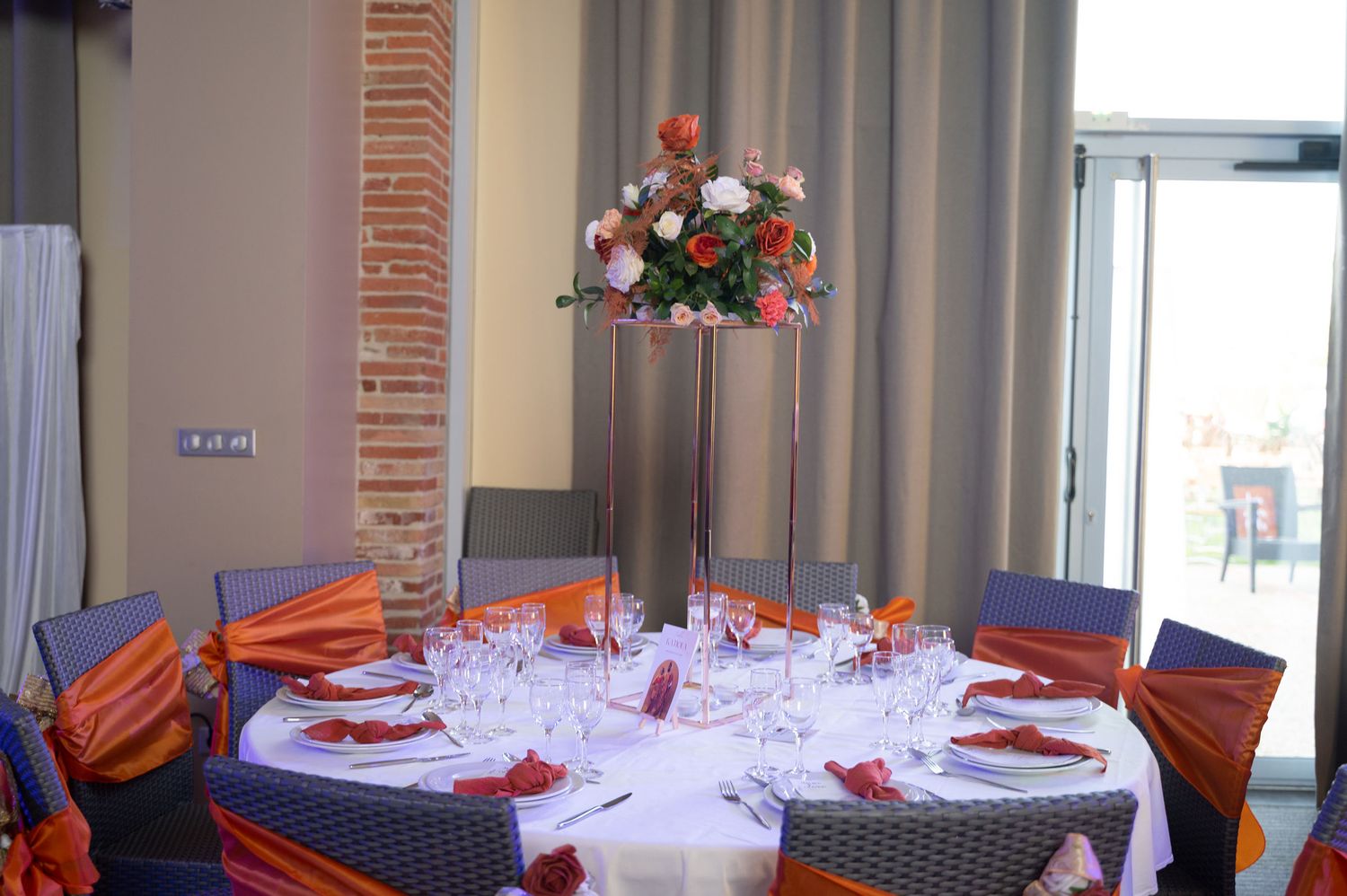 Round wedding reception table with tall floral centerpiece, orange napkins, and wine glasses set elegantly.