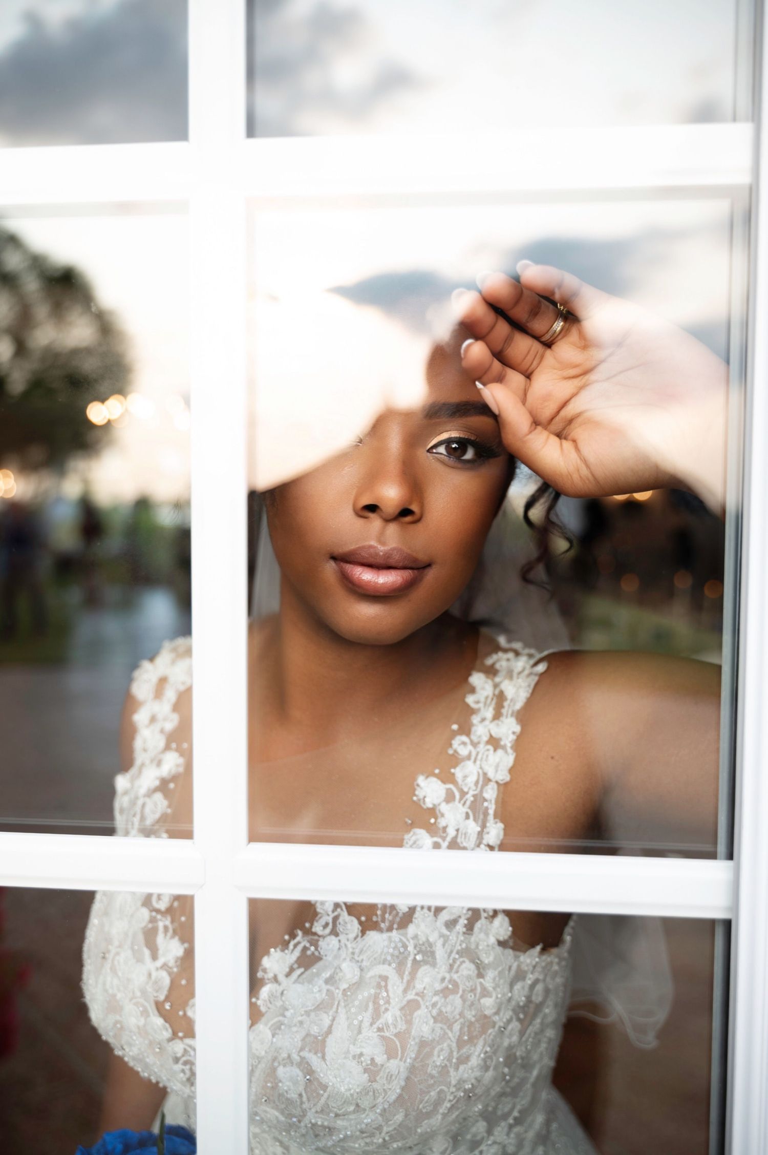 Elegant Black bride in lace wedding gown gazes through a window at golden hour.