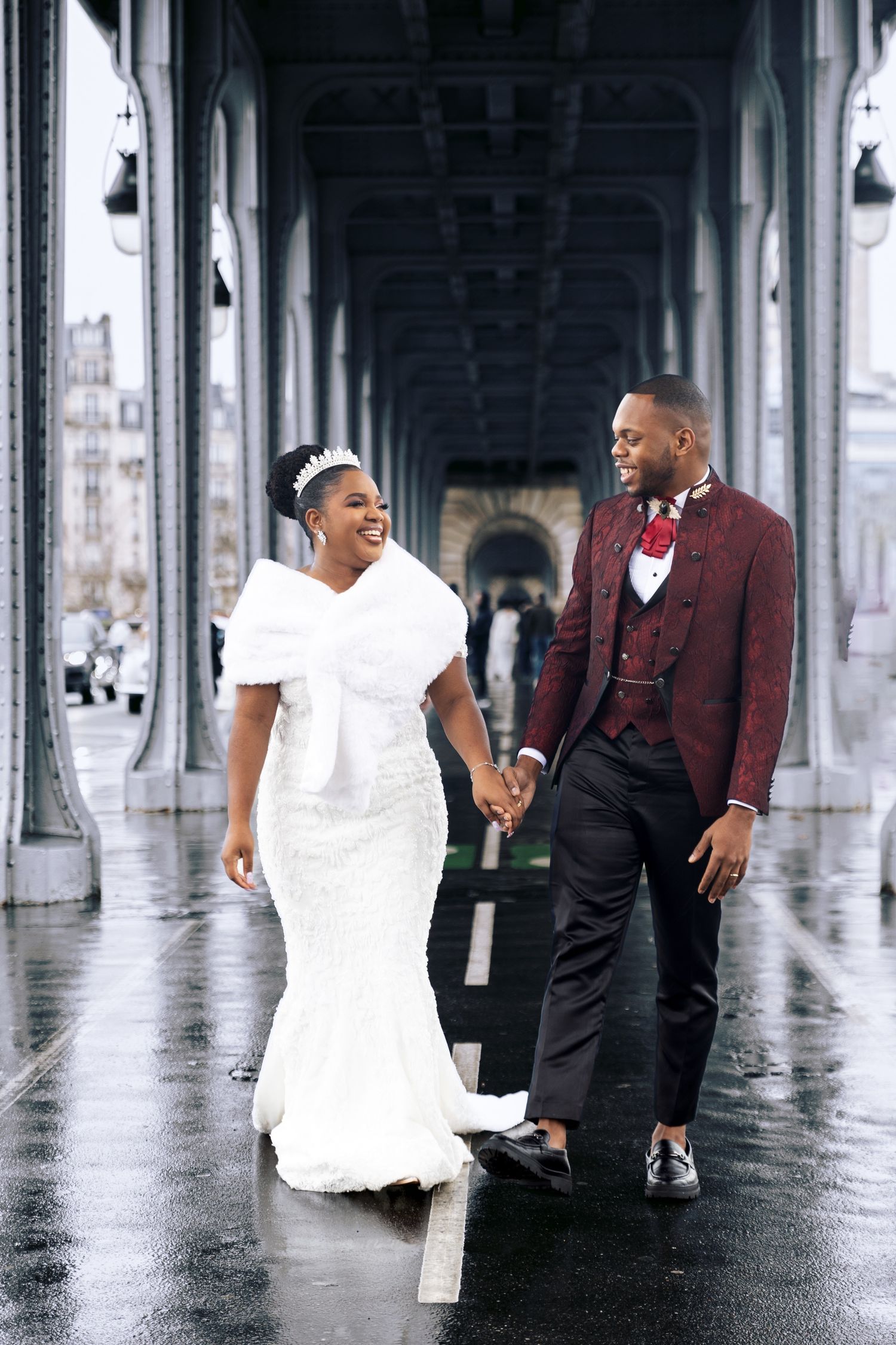 Bride and groom walking hand in hand under a Parisian bridge arcade on a rainy wedding day.