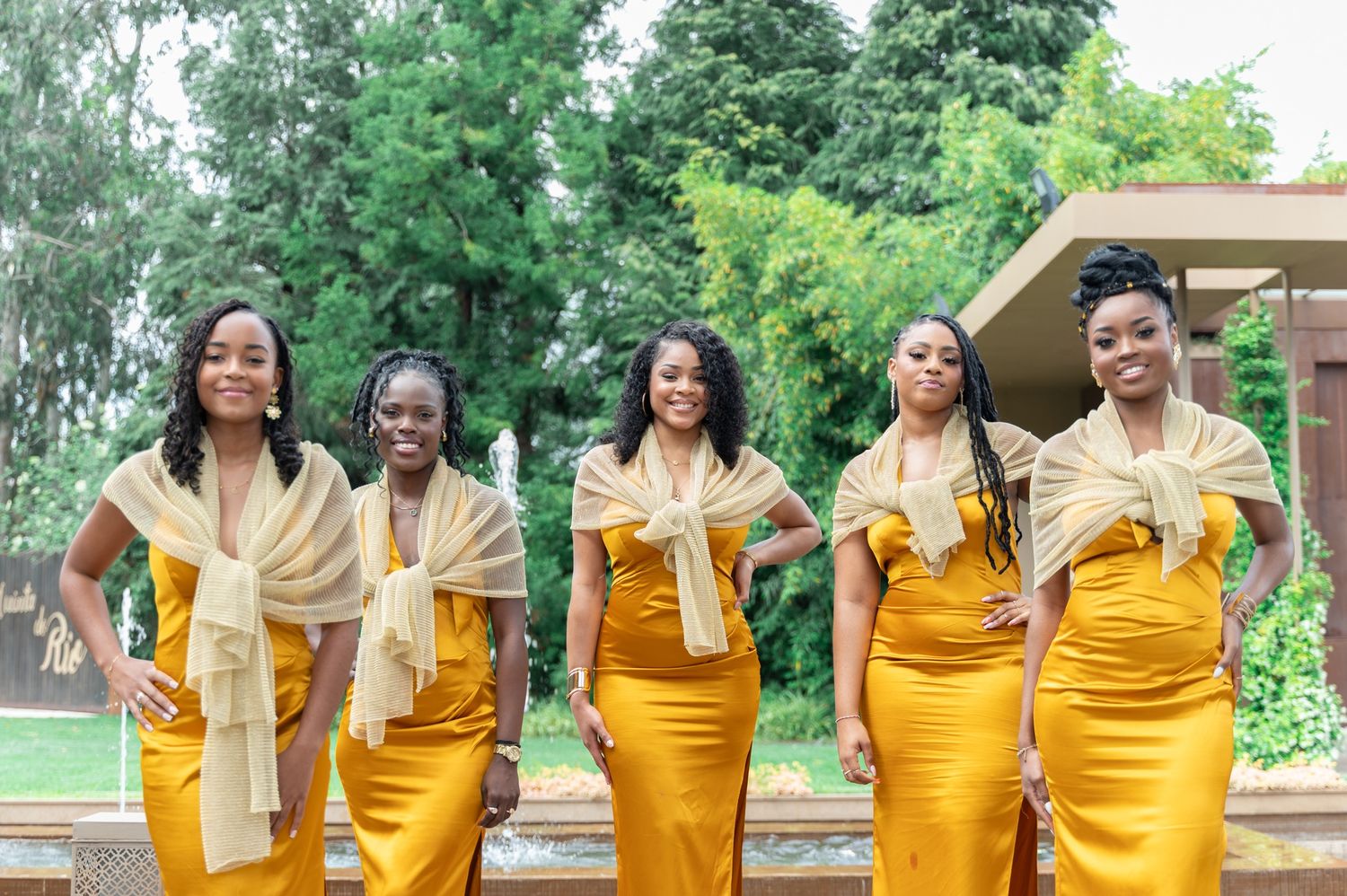 Five bridesmaids in golden yellow mermaid dresses with scarves posing outdoors at a wedding.