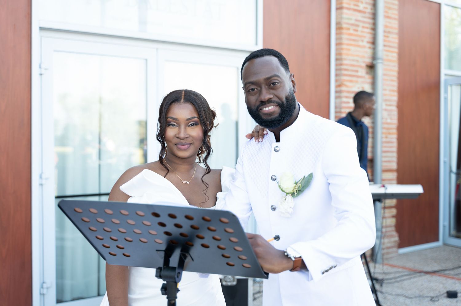 Smiling bride and groom in white wedding outfits standing together at an outdoor wedding ceremony podium.