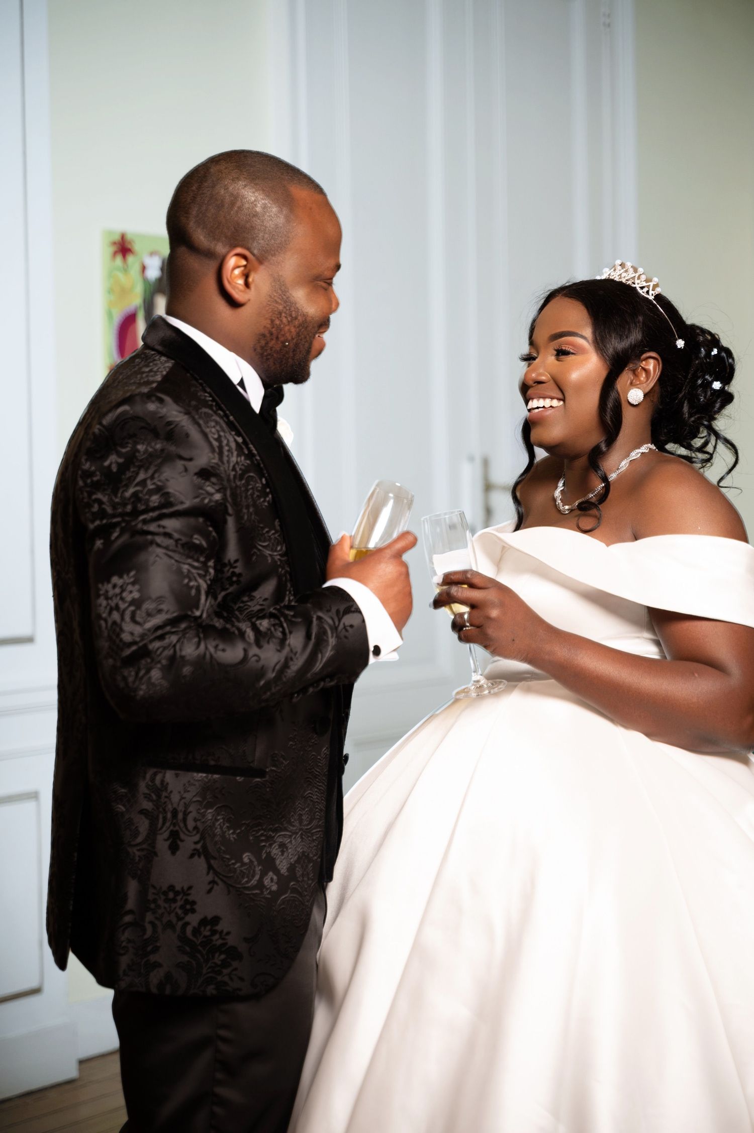 Bride in white off-shoulder ballgown and groom in black tuxedo toast champagne glasses and smile.
