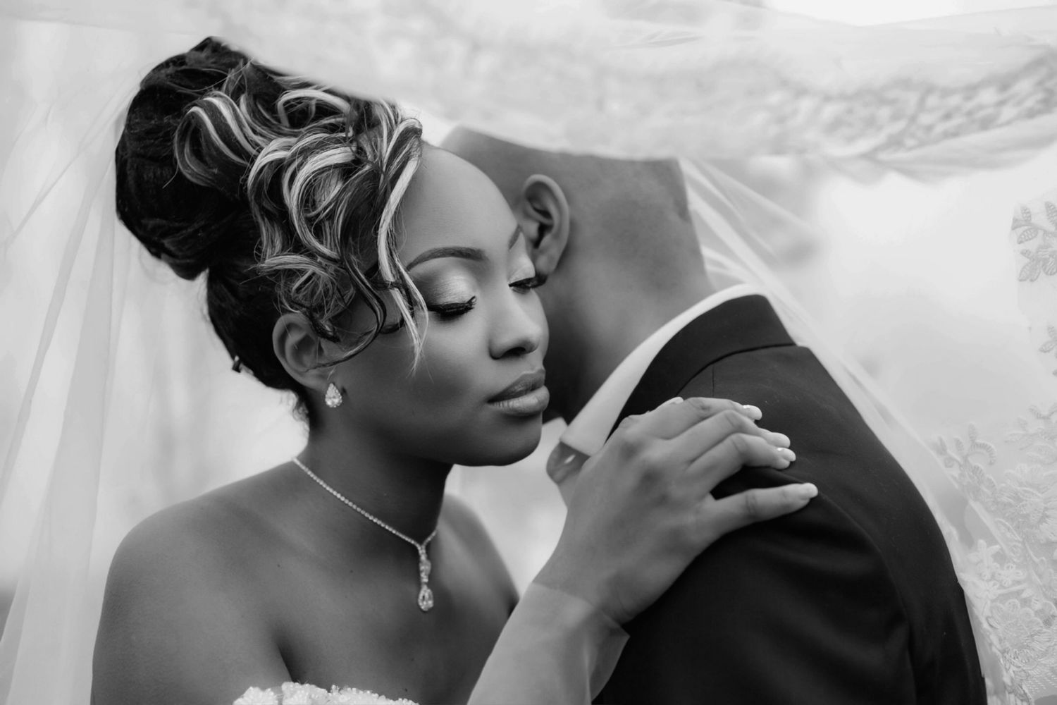 Black and white portrait of a bride and groom sharing a tender kiss under a veil.