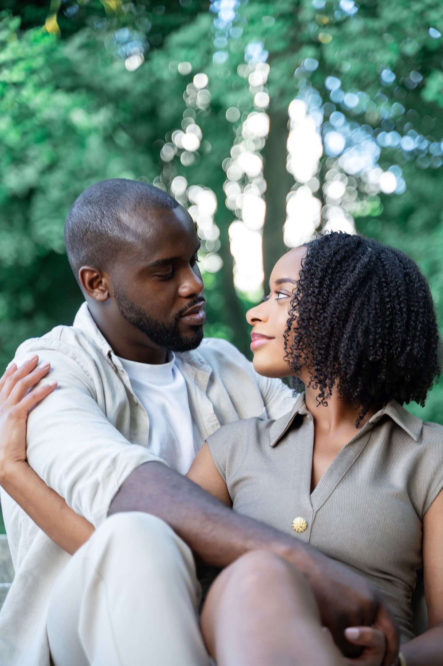 Romantic couple gazing into each others eyes while sitting outdoors among green trees.