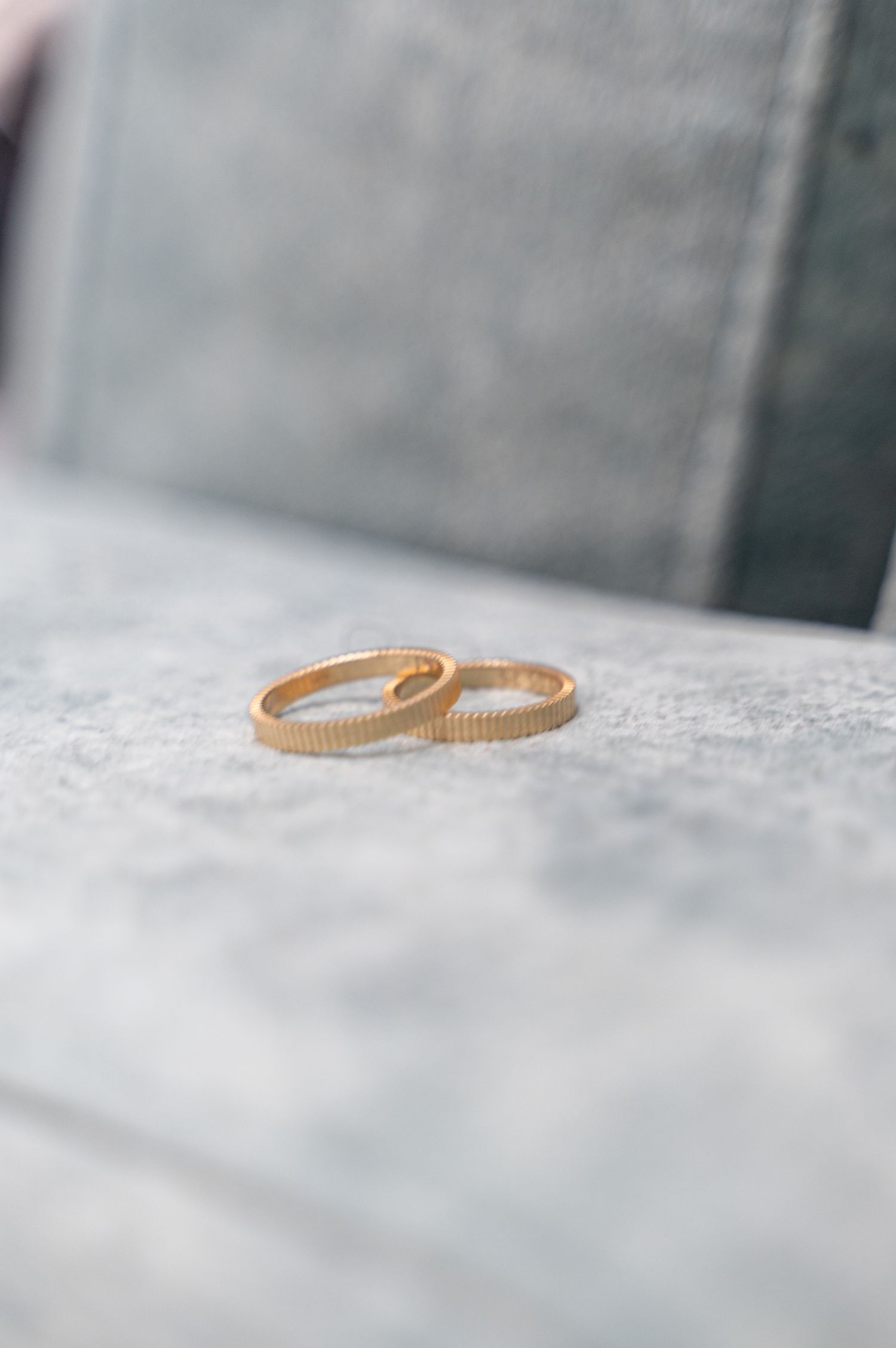 Two matching gold ribbed wedding bands resting on a gray stone surface.