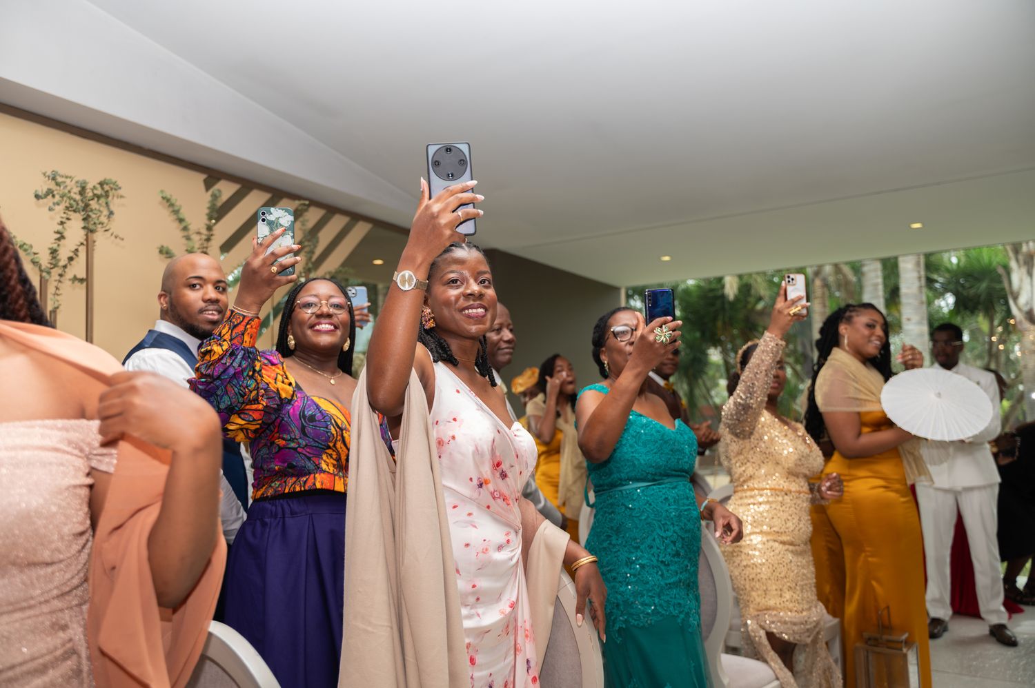 Excited wedding guests in colorful attire celebrate and record the reception on their smartphones.