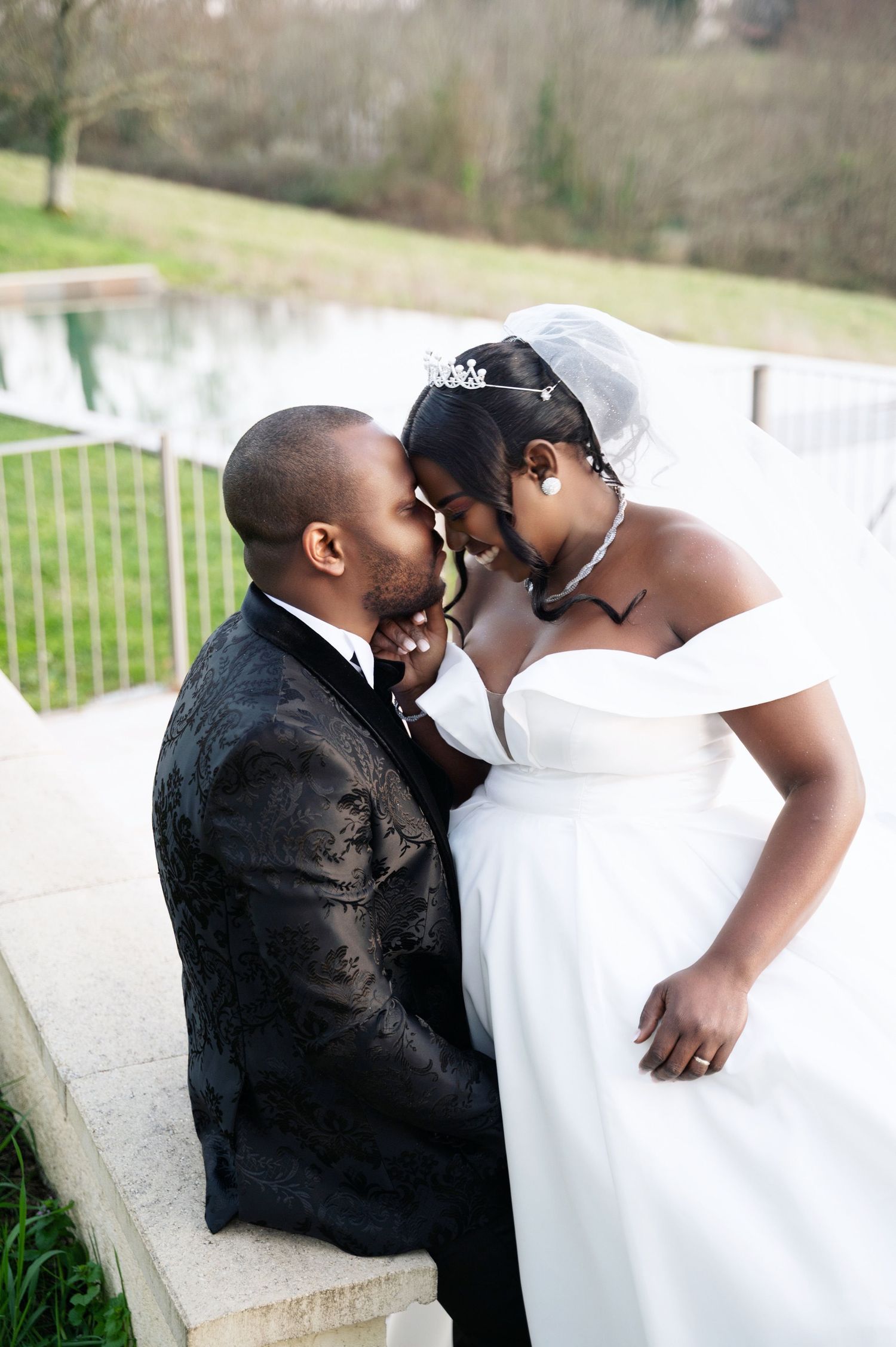 Bride and groom touching foreheads romantically on outdoor terrace with garden backdrop.