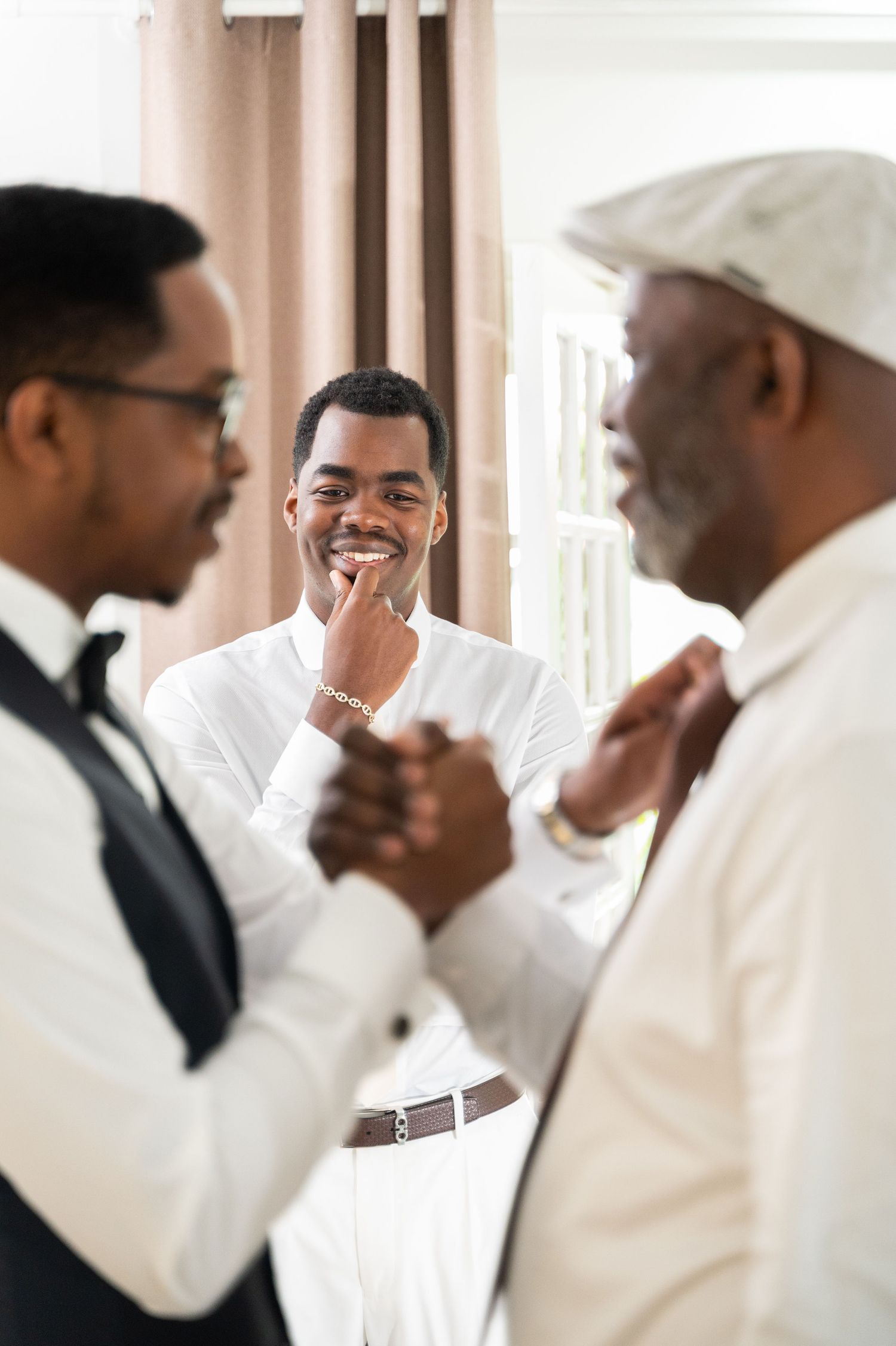 A smiling groom in a white shirt shares a joyful moment with family members while getting ready for his wedding.