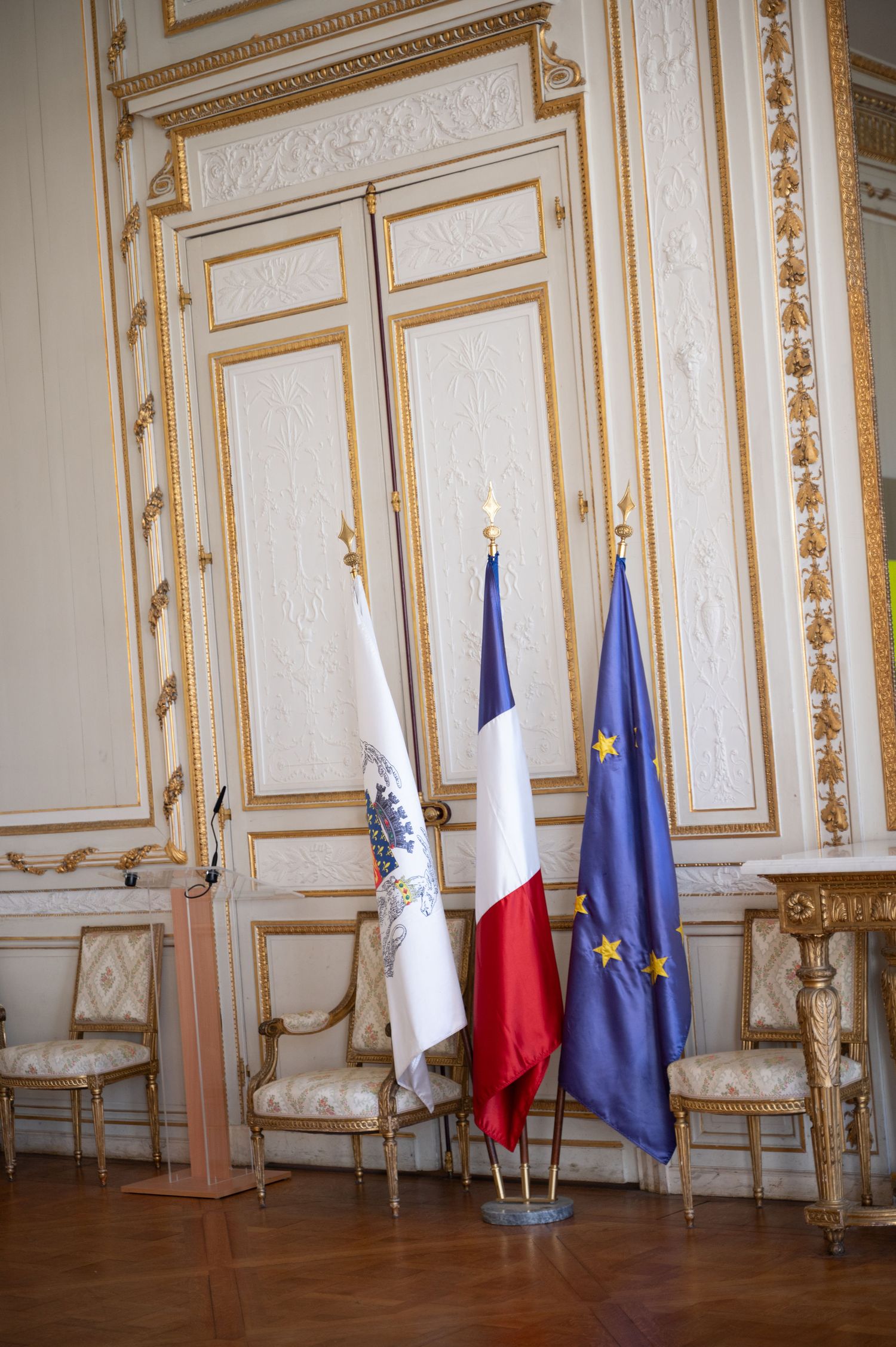 French and European Union flags displayed in ornate gold and white ceremonial room.
