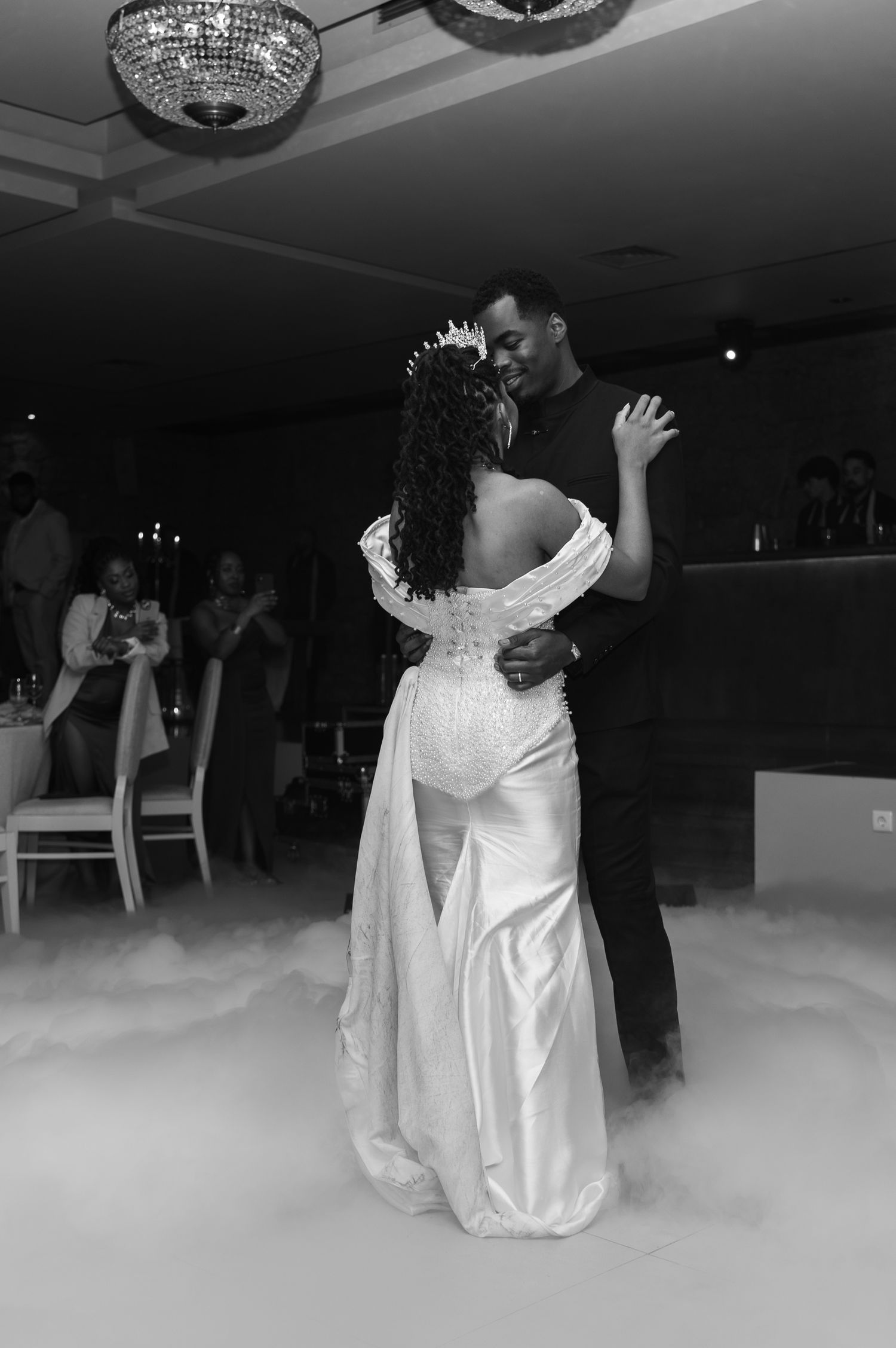 Black and white photo of bride and groom sharing romantic first dance on fog-covered dance floor.