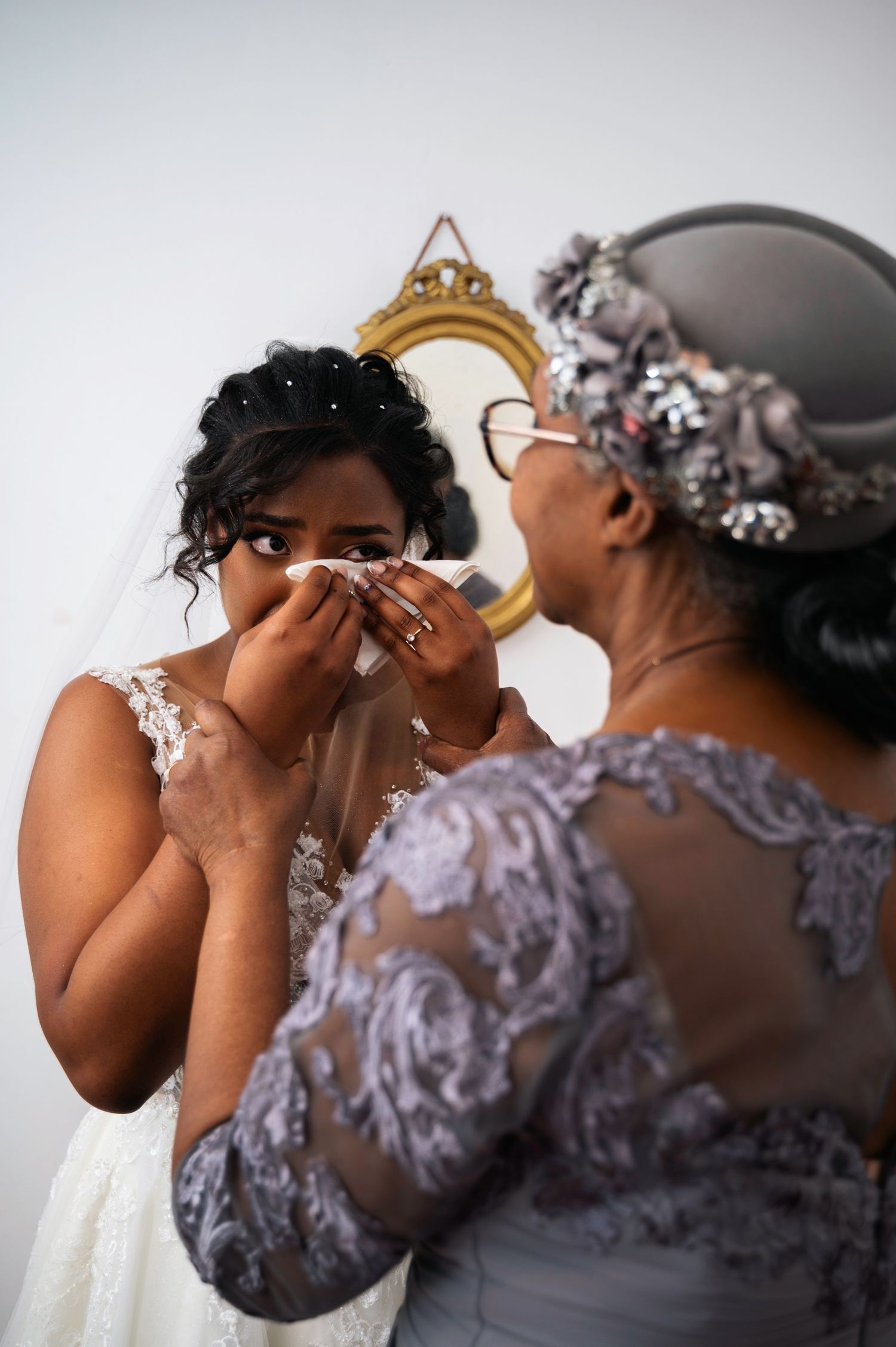 Emotional bride wiping tears as an older woman in silver lace dress comforts her.