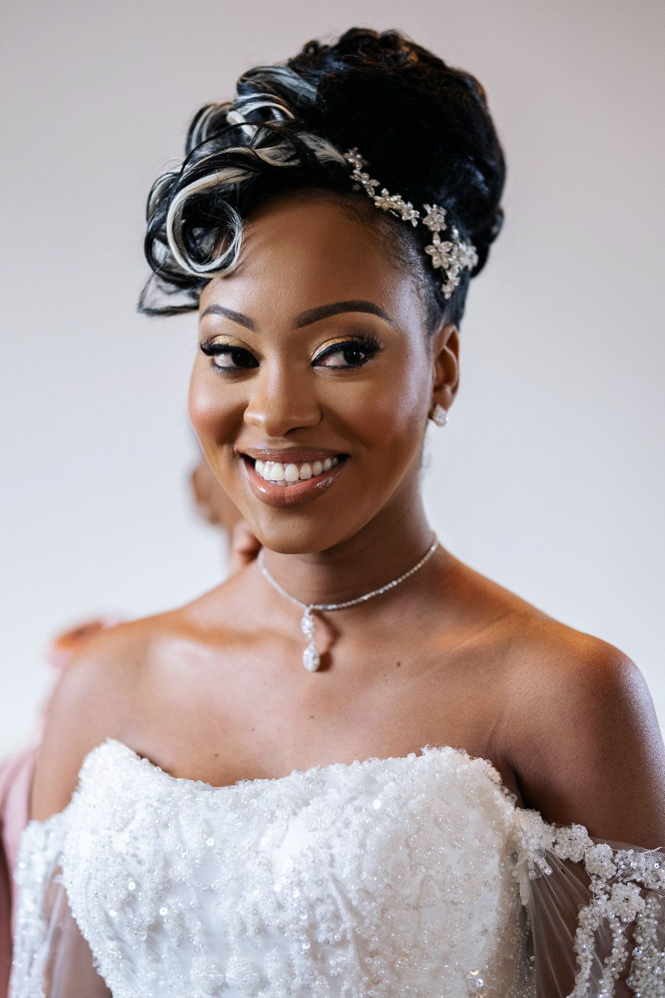Beautiful Black bride smiling in a strapless white lace gown with an elegant updo and crystal accessories.