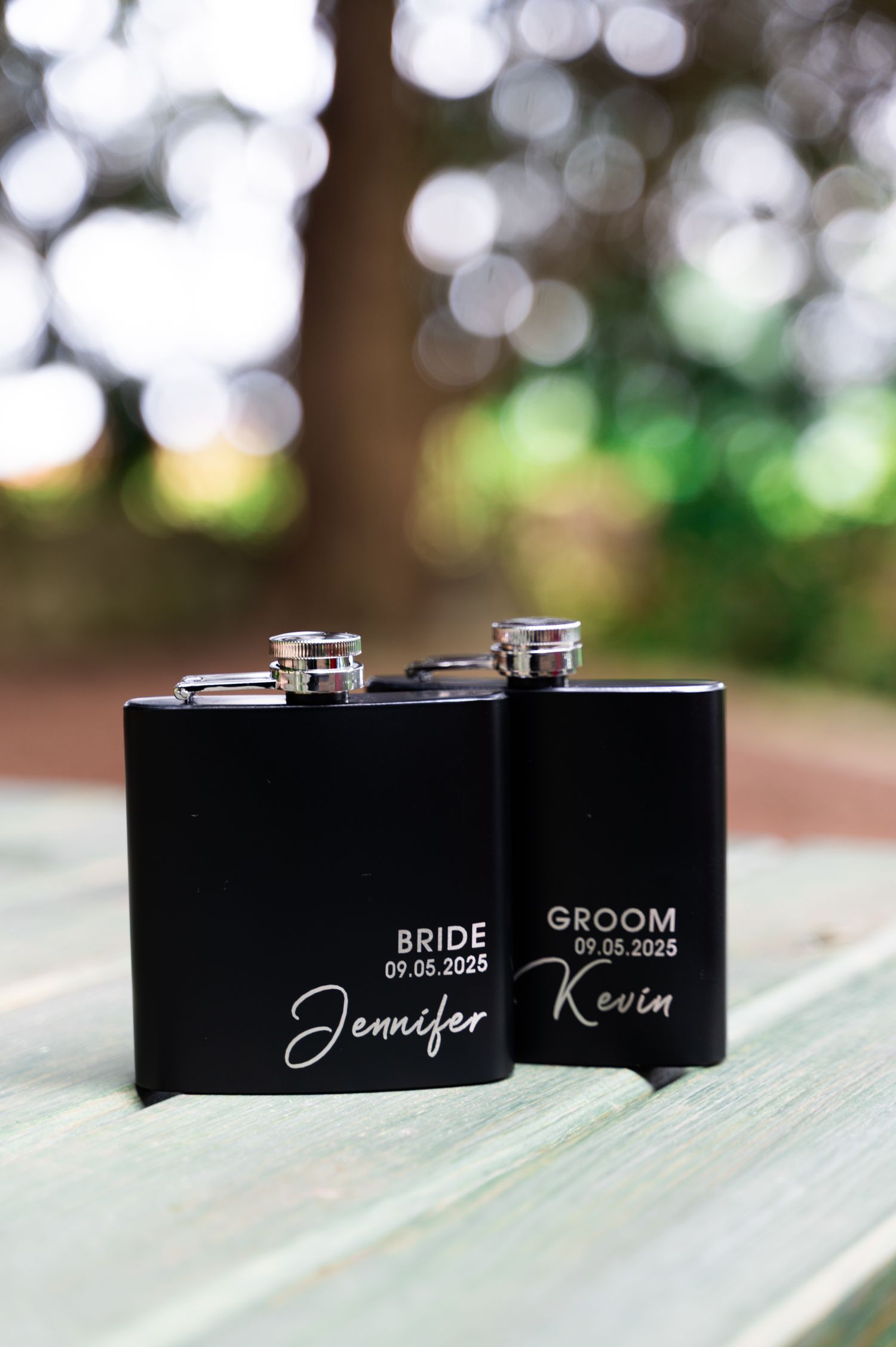 Personalized black metal flasks engraved with Bride Jennifer and Groom Kevin dated 09.05.2025.