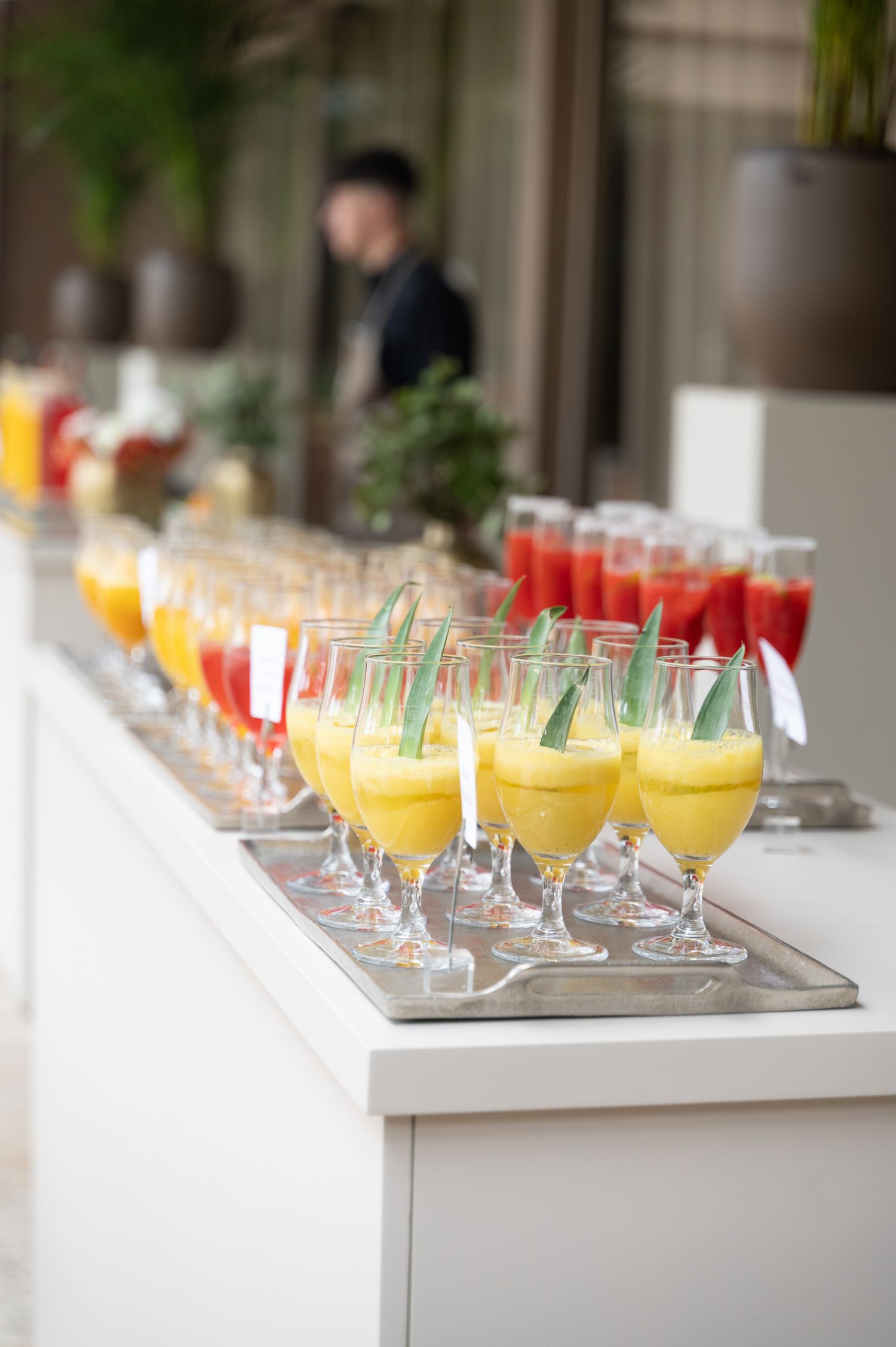 Colorful mango and strawberry cocktails lined up on white bar at wedding reception.